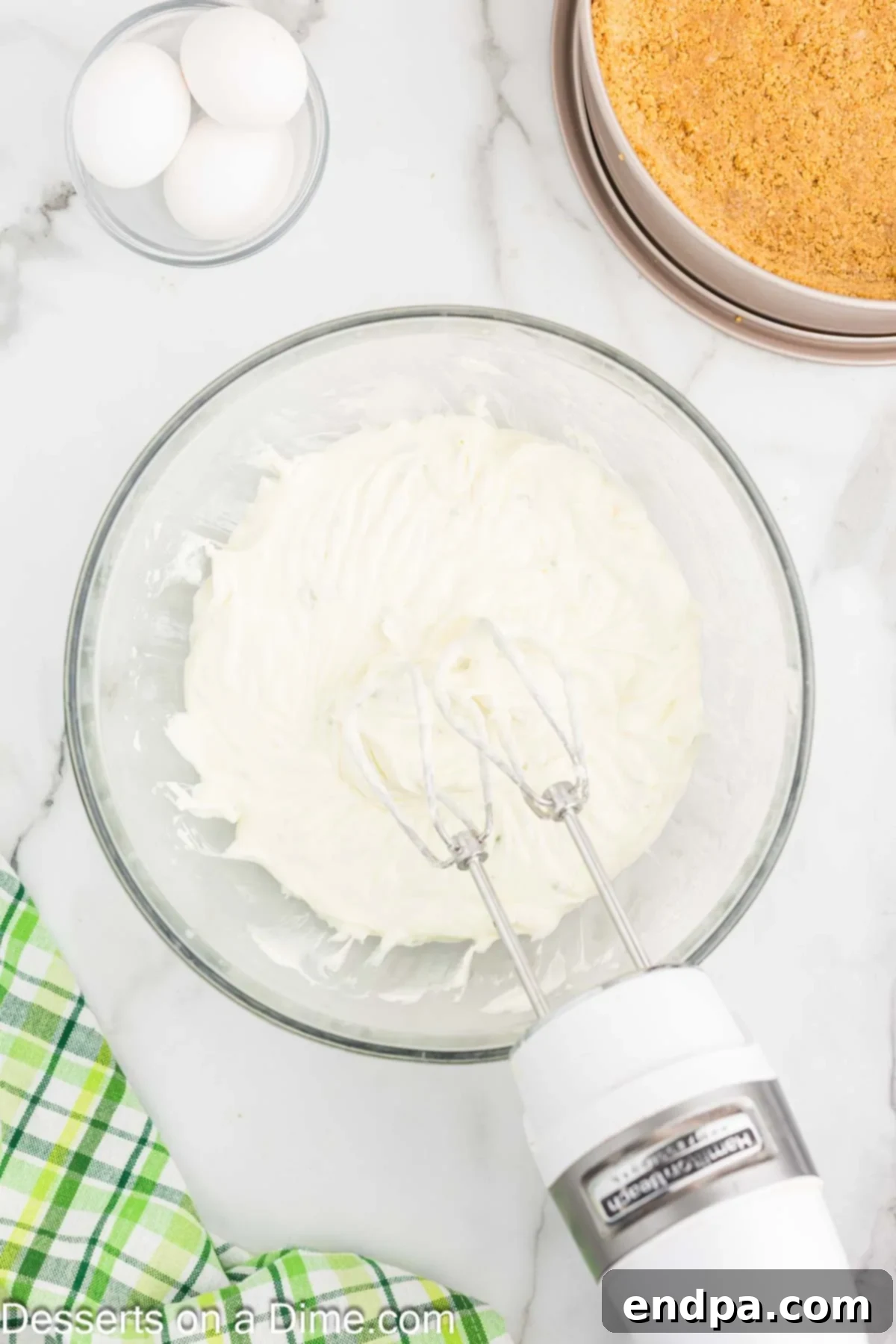 Cream cheese mixture being beaten smooth in a large mixing bowl with a hand mixer.