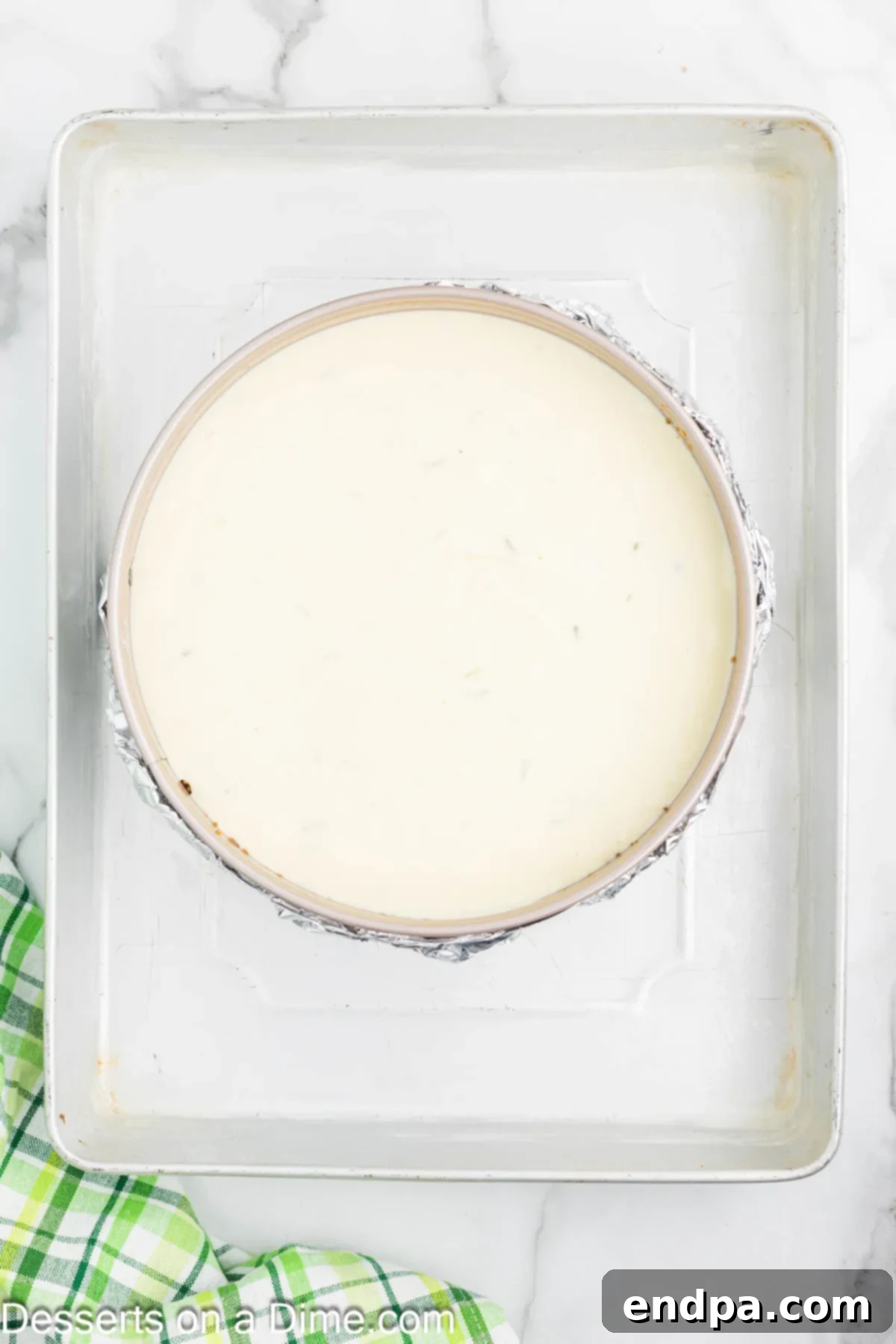 Key Lime Cheesecake in a springform pan, placed inside a larger baking dish with hot water for a water bath.