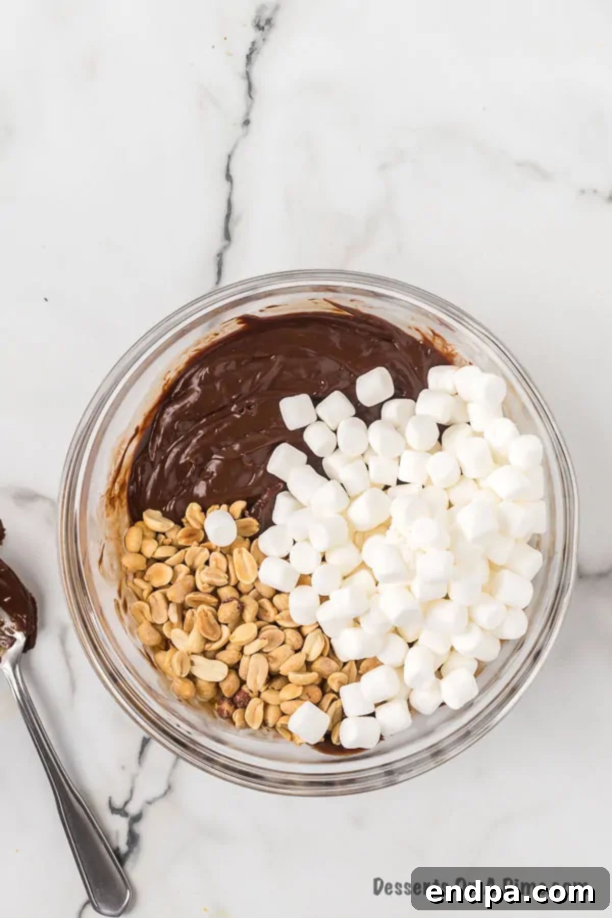 Marshmallows and nuts folded into mixture. A close-up view of mini marshmallows and salted peanuts being gently folded into the chocolate fudge mixture.