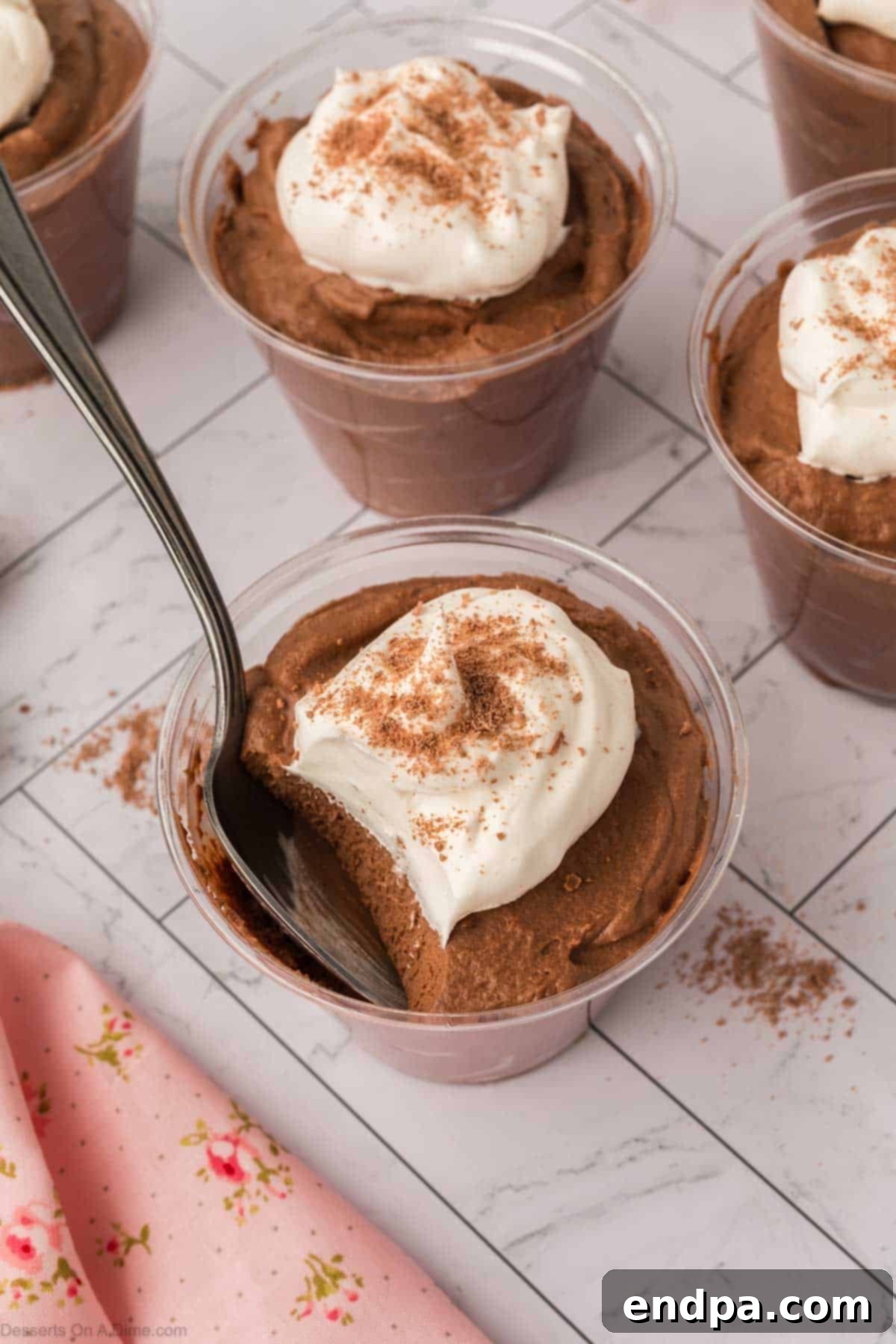 Close-up of a chocolate mousse cup garnished with fresh whipped cream and chocolate shavings.