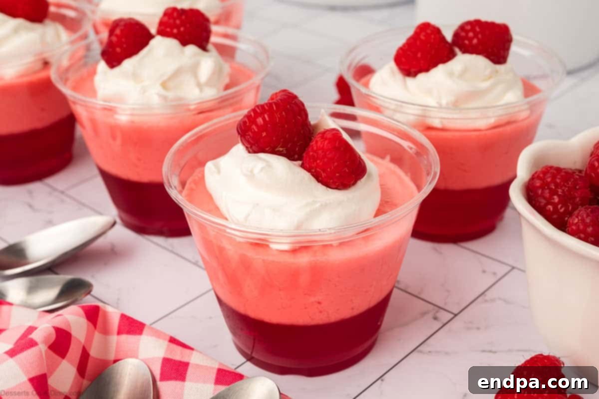 Layered Gelatin Delight 2 Jello Parfait in clear cups topped with fresh raspberries and whipped cream, ready to be served.