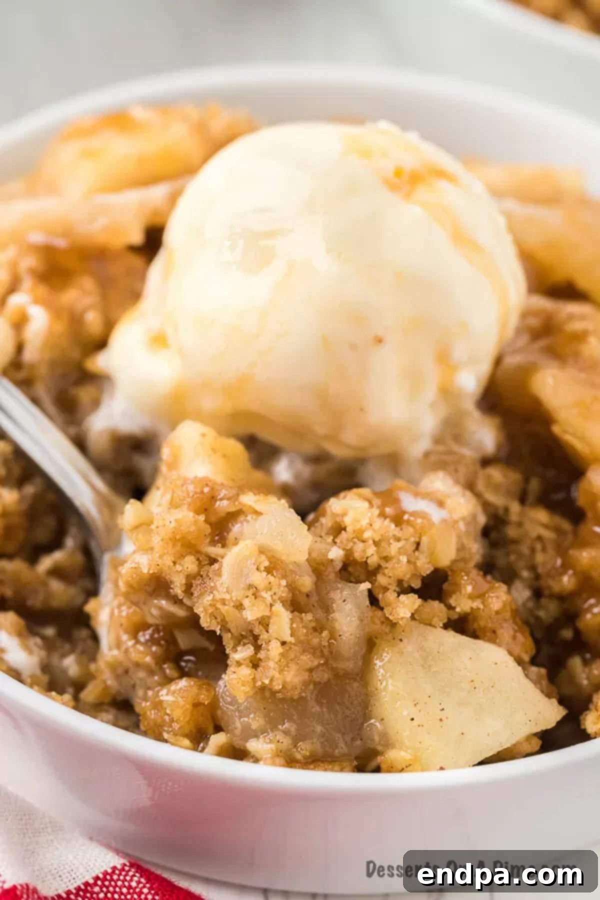 Buttery Oat Apple Crisp 12 A close-up of apple crisp in a bowl topped with melting vanilla ice cream.