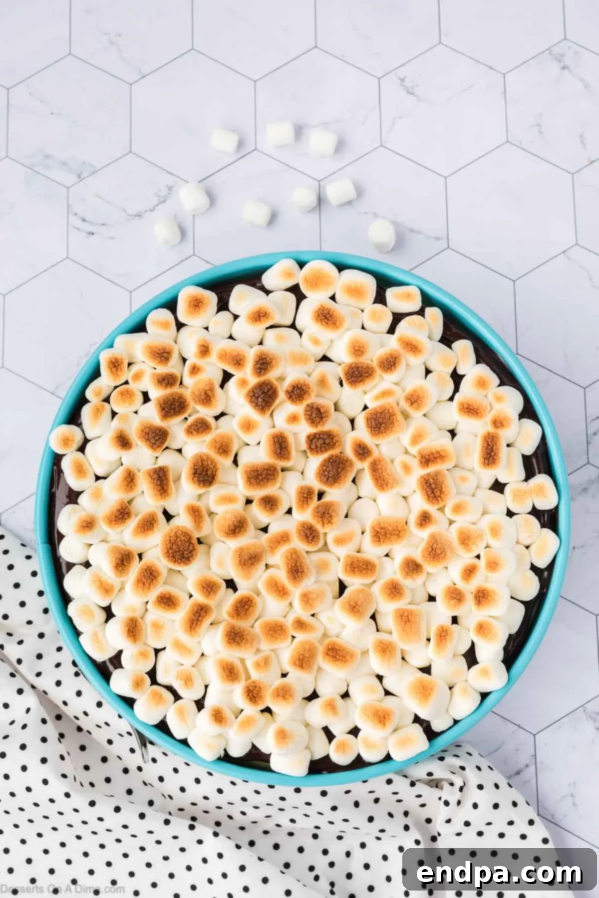 The S'mores Cheesecake with mini marshmallows perfectly broiled to a golden-brown and slightly charred finish, creating a delicious and visually appealing topping.