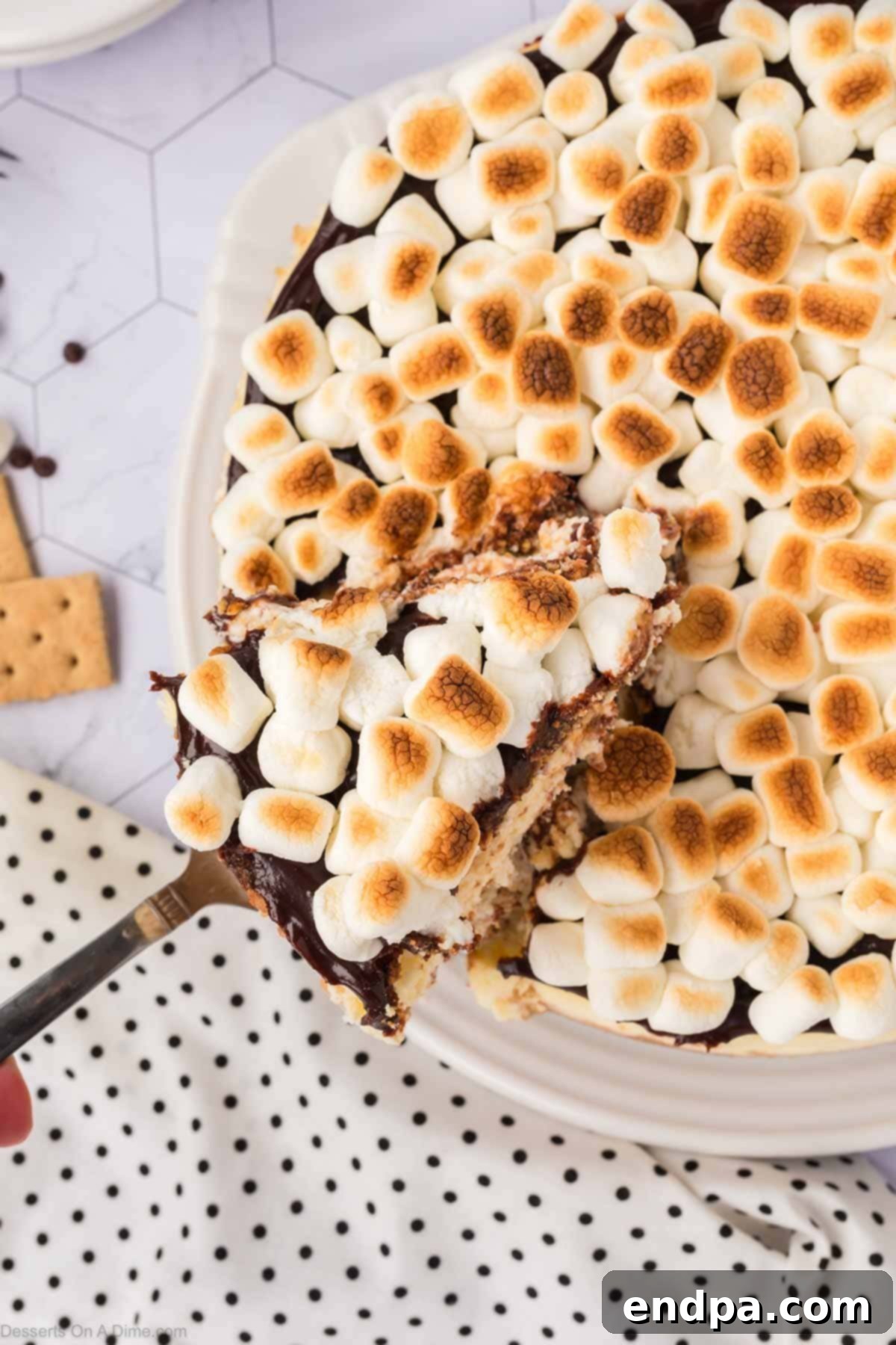 A S'mores cheesecake being expertly sliced with a knife, revealing the distinct layers of crust, chocolate cheesecake, and toasted marshmallow topping, ready for serving.