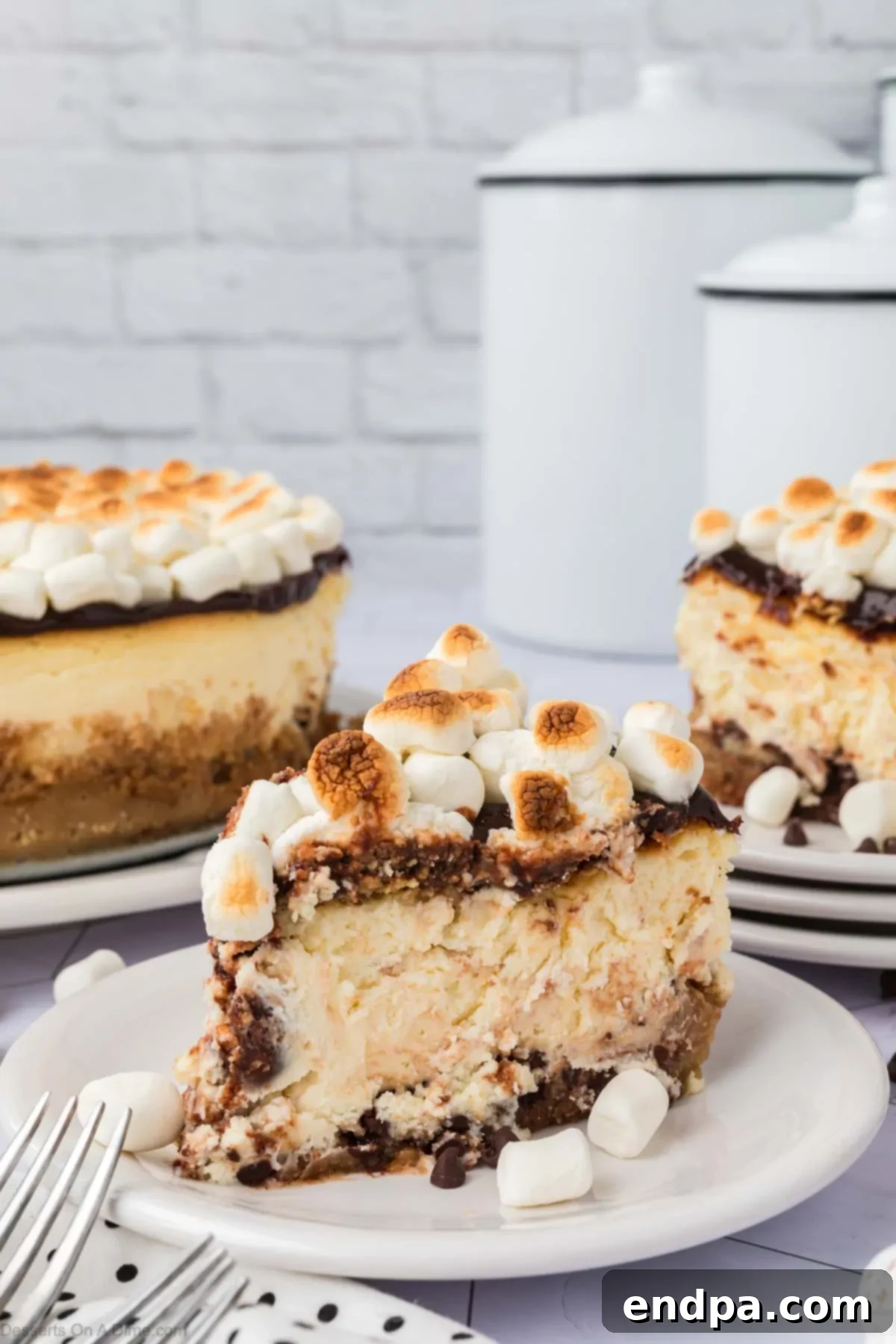 A perfect slice of S'mores cheesecake served on a white plate, showcasing the graham cracker crust, dense chocolate filling, and fluffy toasted marshmallow topping. It's garnished with a small piece of chocolate.