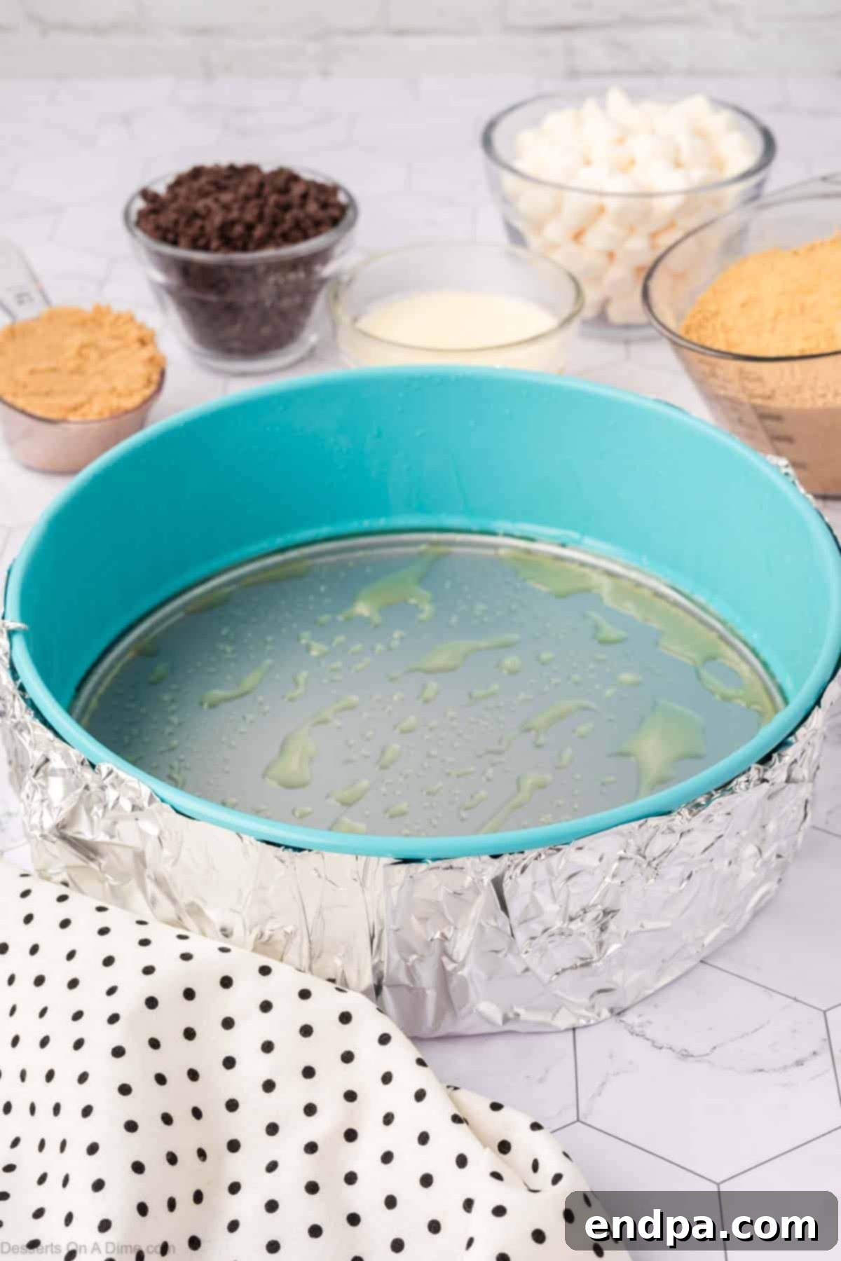 A 9-inch springform pan with its exterior meticulously wrapped in aluminum foil, ready for the water bath. This step is crucial for preventing water seepage during baking.