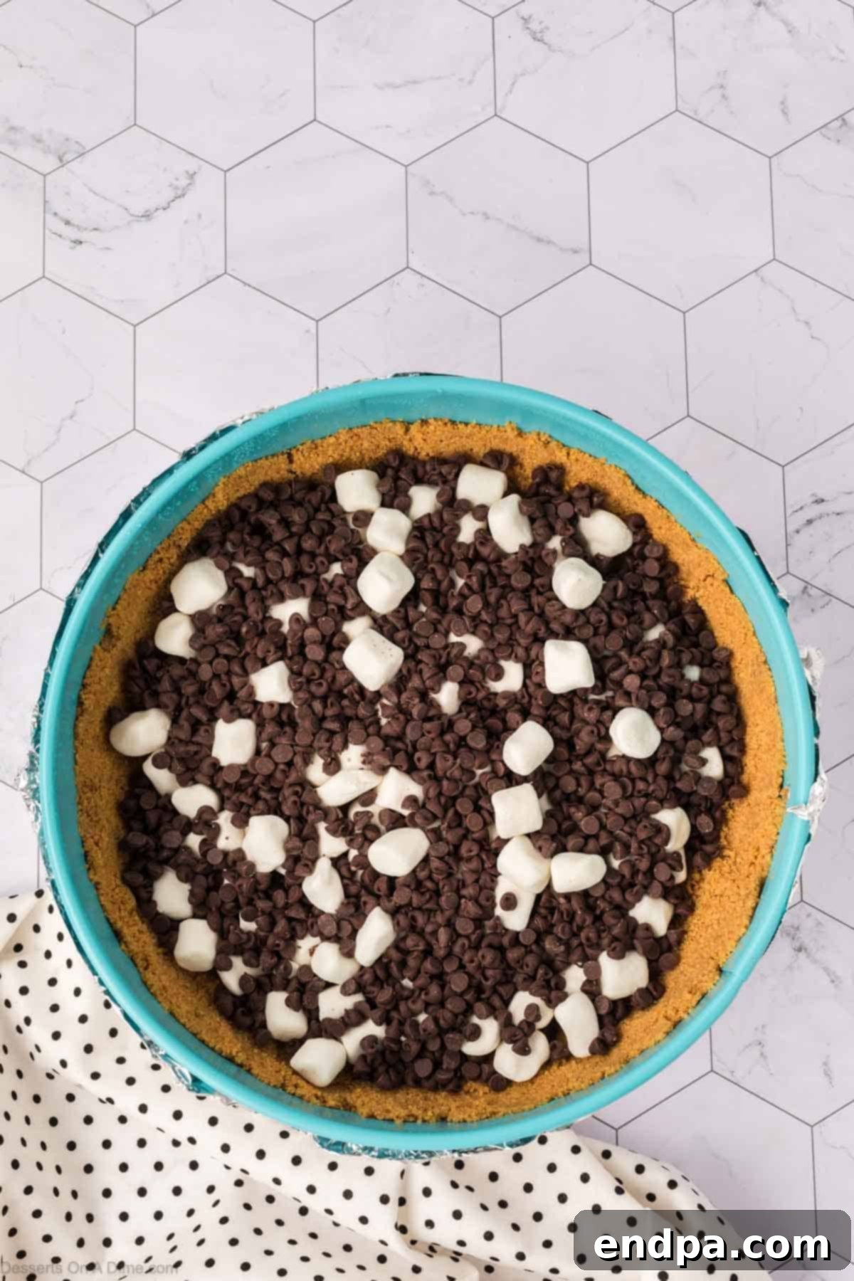 Mini chocolate chips and mini marshmallows generously sprinkled over the cooled graham cracker crust in the springform pan, forming the 's'mores' foundation.