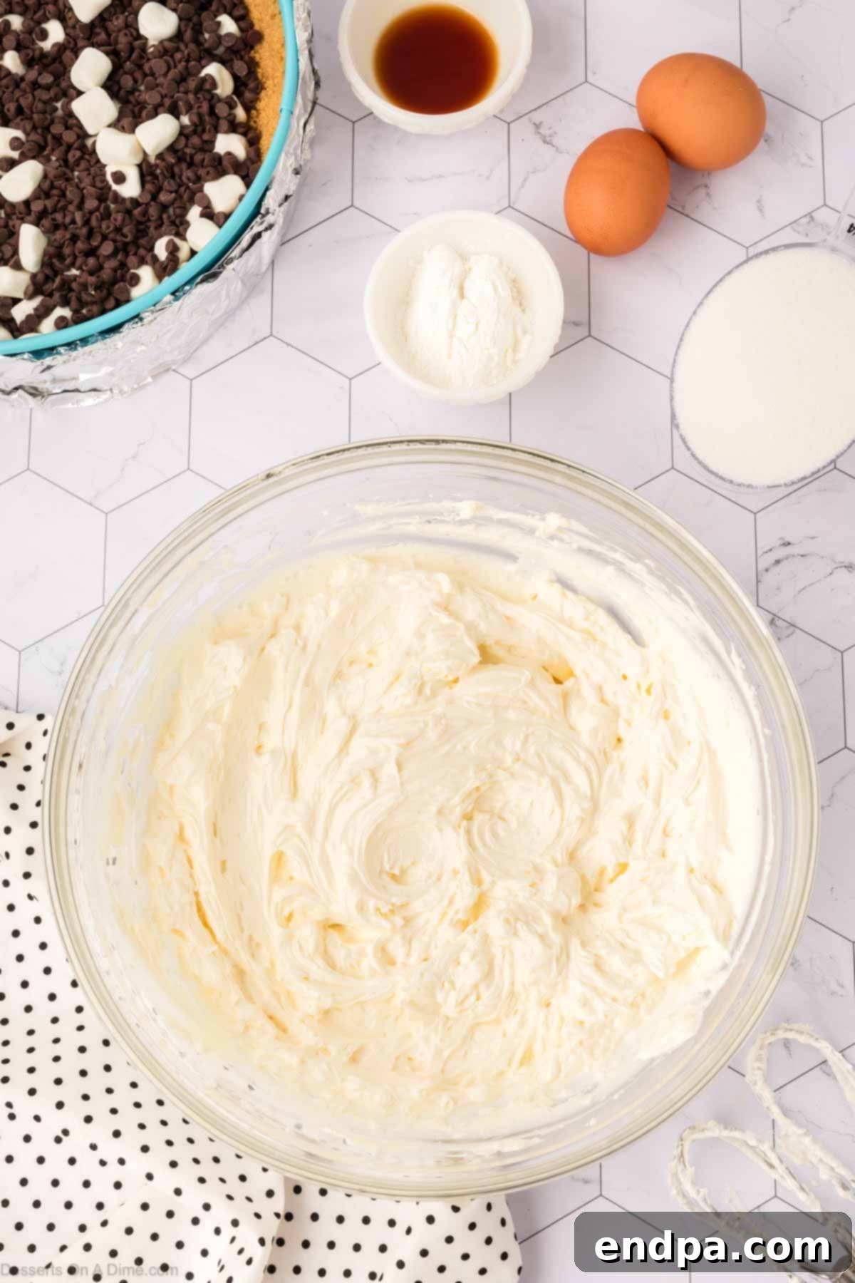 Softened cream cheese being beaten until light and fluffy in the bowl of an electric stand mixer with a paddle attachment, showing the smooth, aerated texture.