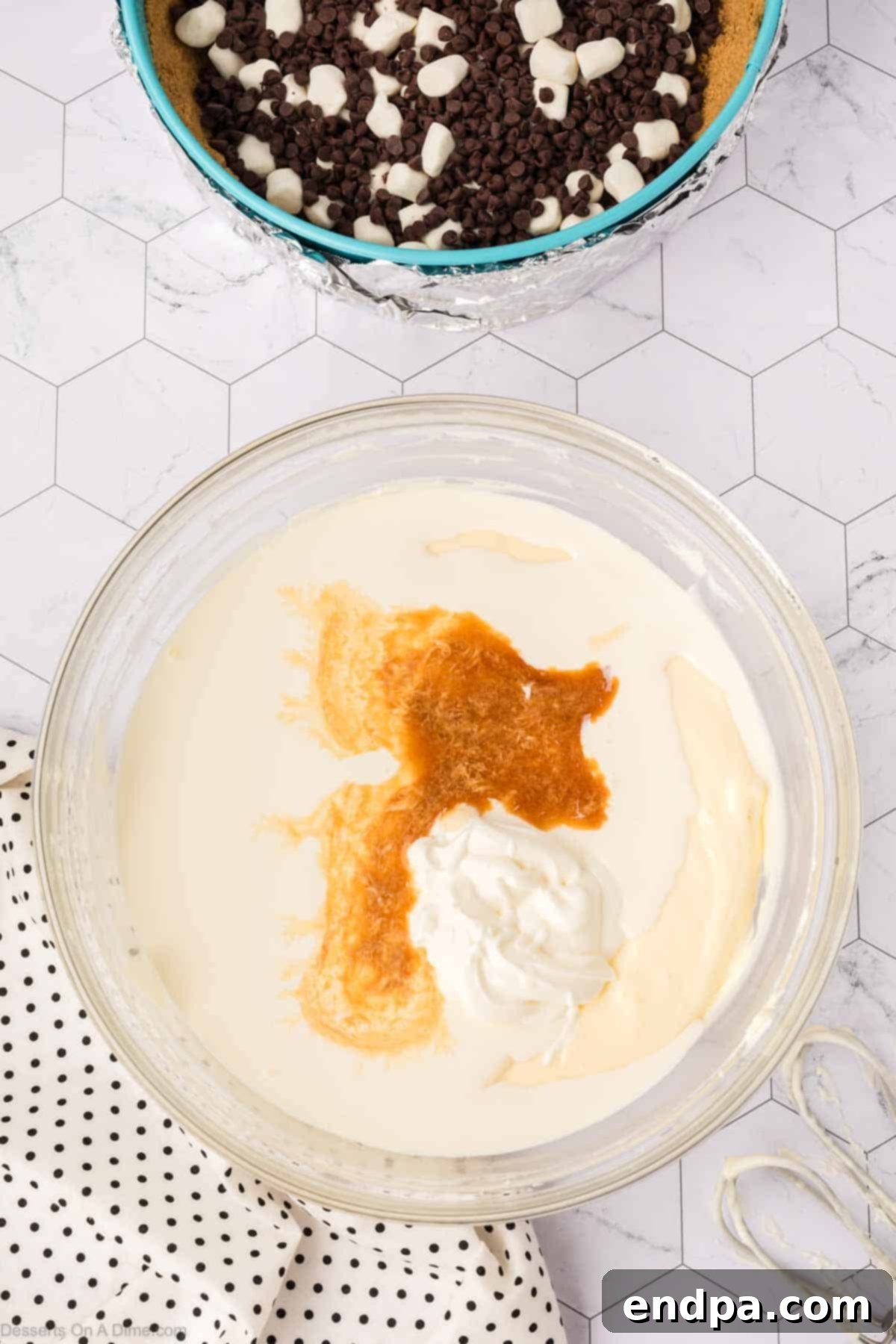 Vanilla extract, sour cream, and eggs being added to the light and fluffy cream cheese mixture in an electric mixer, ready for blending into the cheesecake batter.