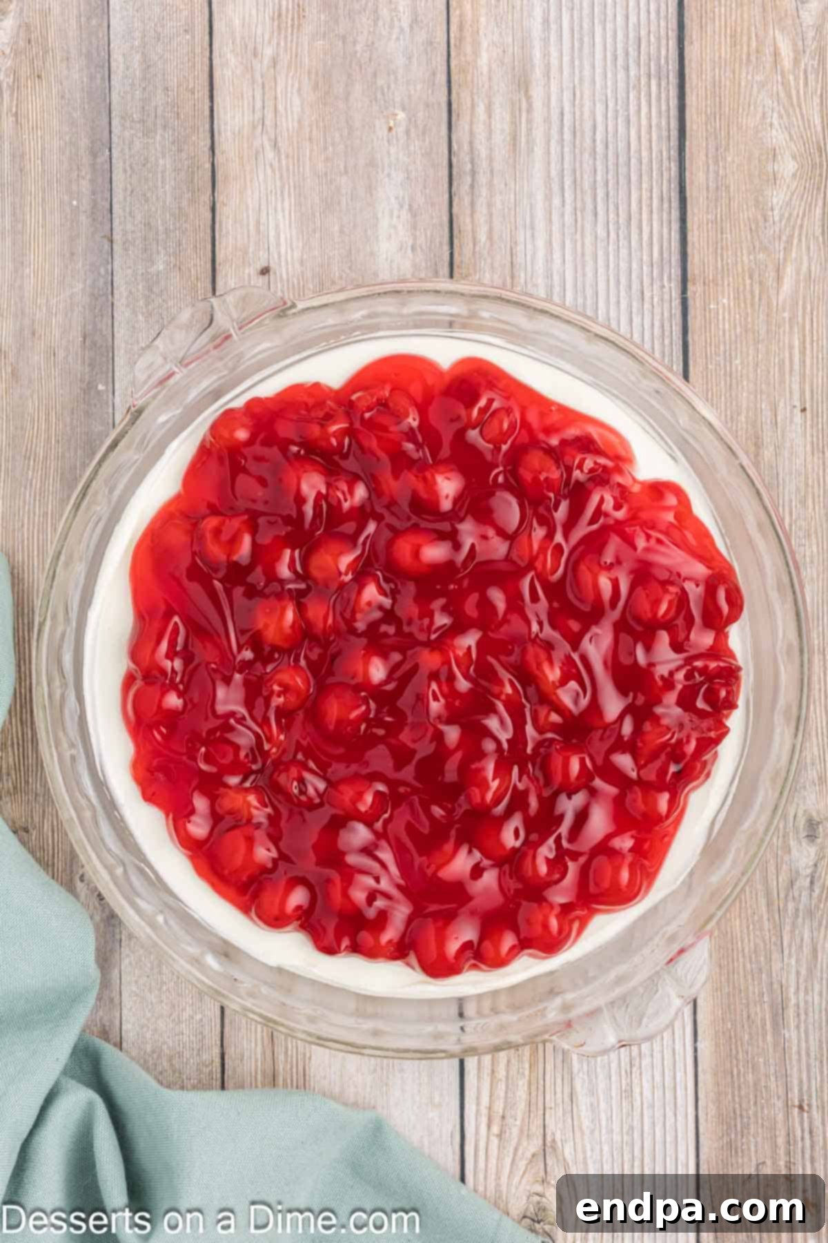 Luscious Cherry Cheesecake Dip 7 Cherry pie filling being spread over the creamy cheesecake mixture in a serving dish.