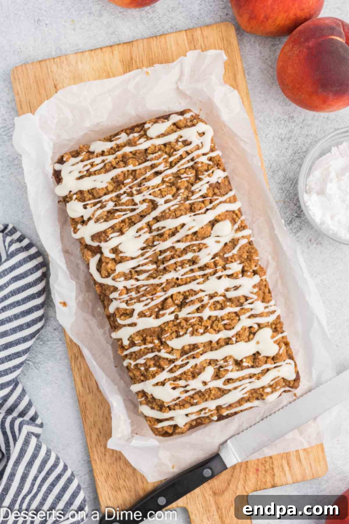 A beautifully glazed loaf of peach bread, with a smooth vanilla glaze cascading over its streusel topping, ready to be sliced and served.