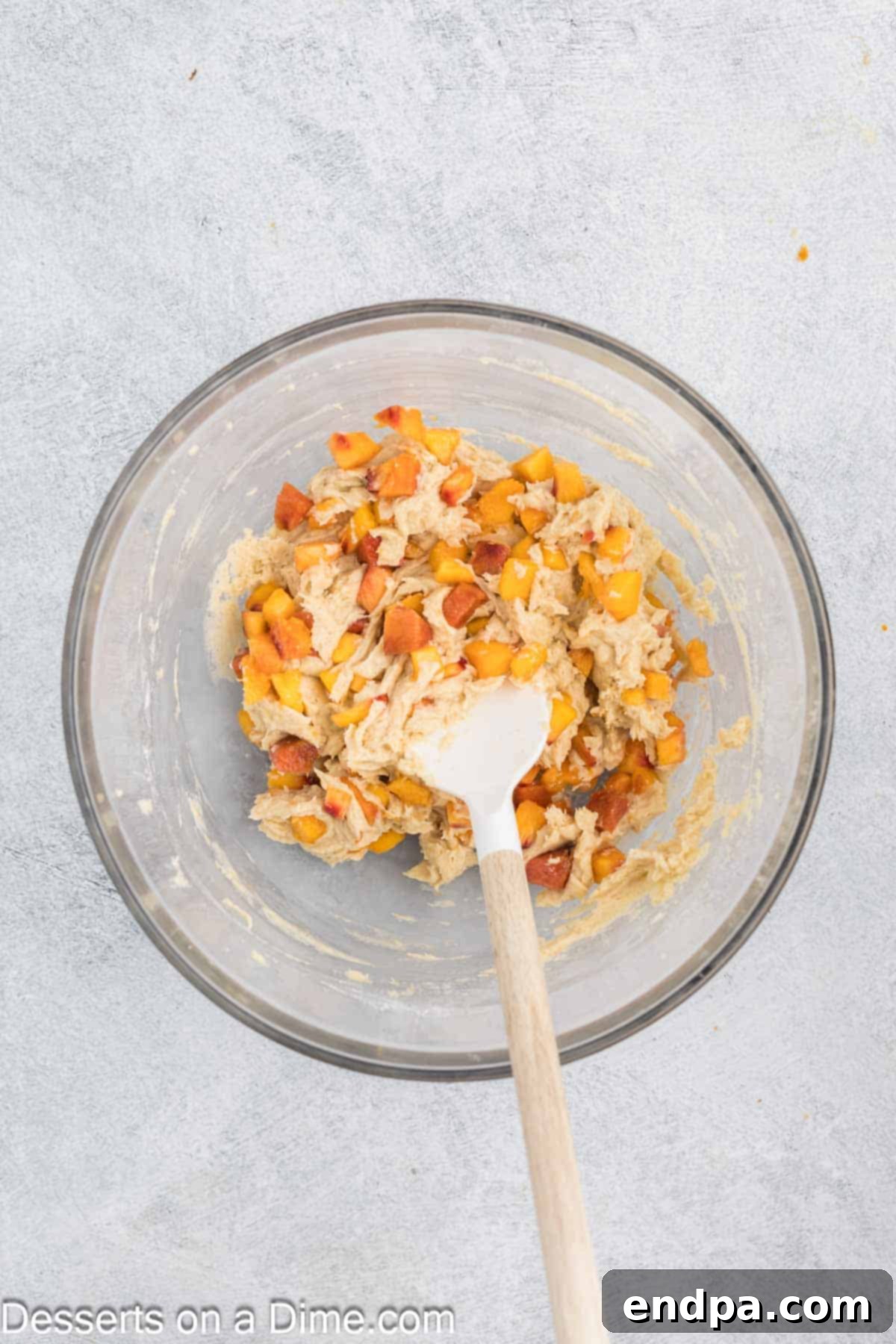 Peach bread batter in a bowl after combining wet and dry ingredients, with fresh, diced peaches gently folded in using a spatula.