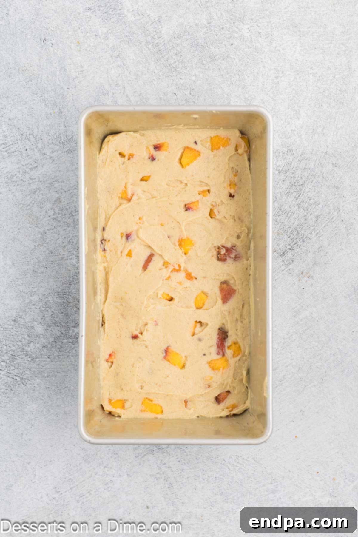 Smooth peach bread batter spread evenly into a prepared 9x5-inch loaf pan, ready for the streusel topping.