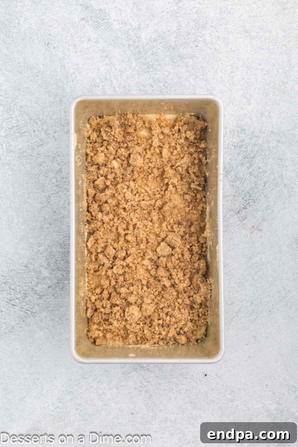 A loaf pan filled with peach bread batter, generously topped with an even layer of streusel, ready for baking.