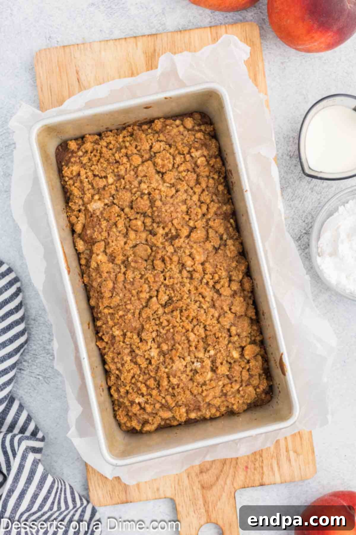A golden-brown loaf of baked peach bread resting in its pan on a wire rack, cooling down before being glazed.