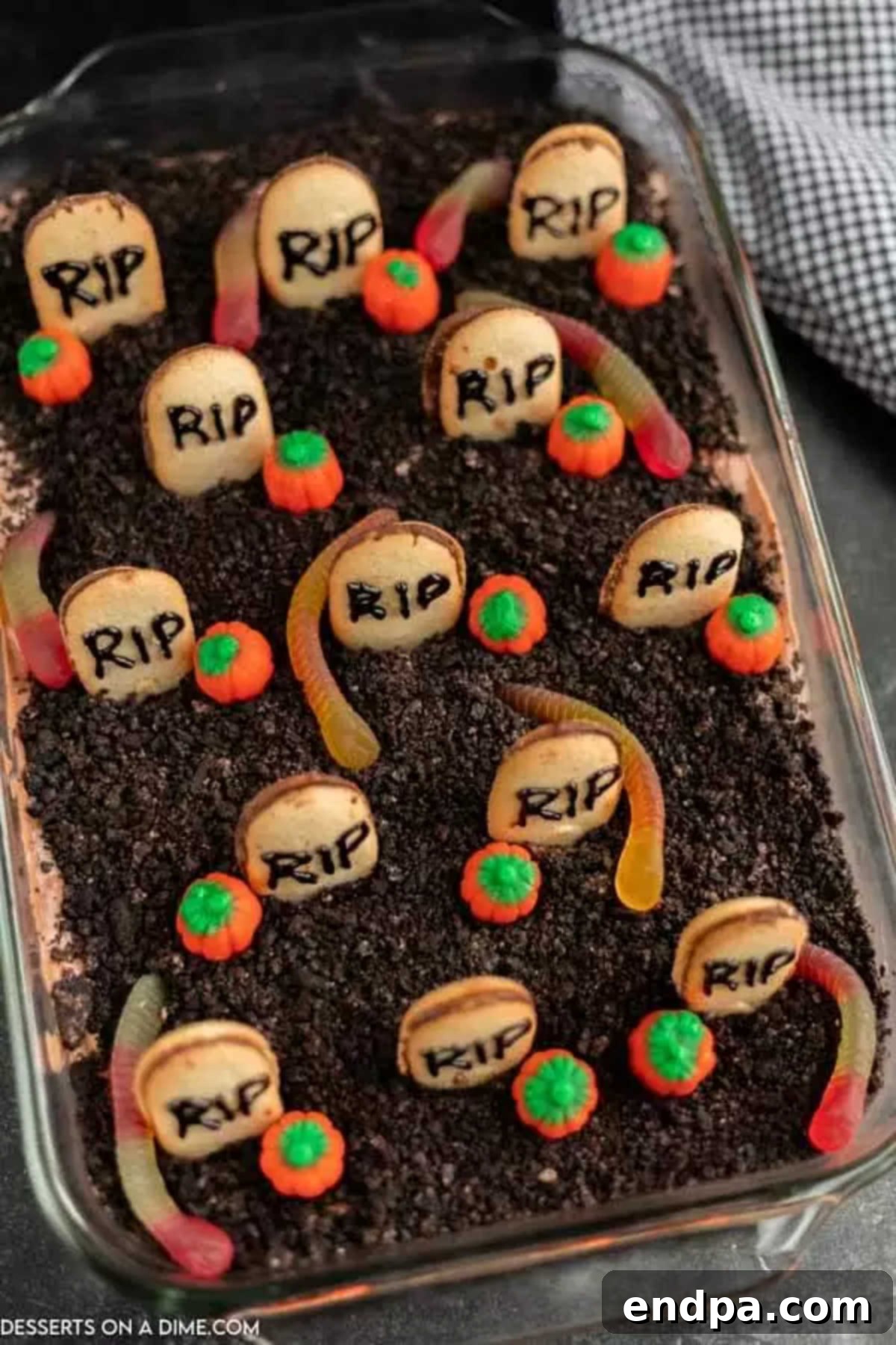 Halloween Dirt Cake in a baking dish ready to serve, adorned with crushed Oreos, gummy worms, candy pumpkins, and tombstone cookies.