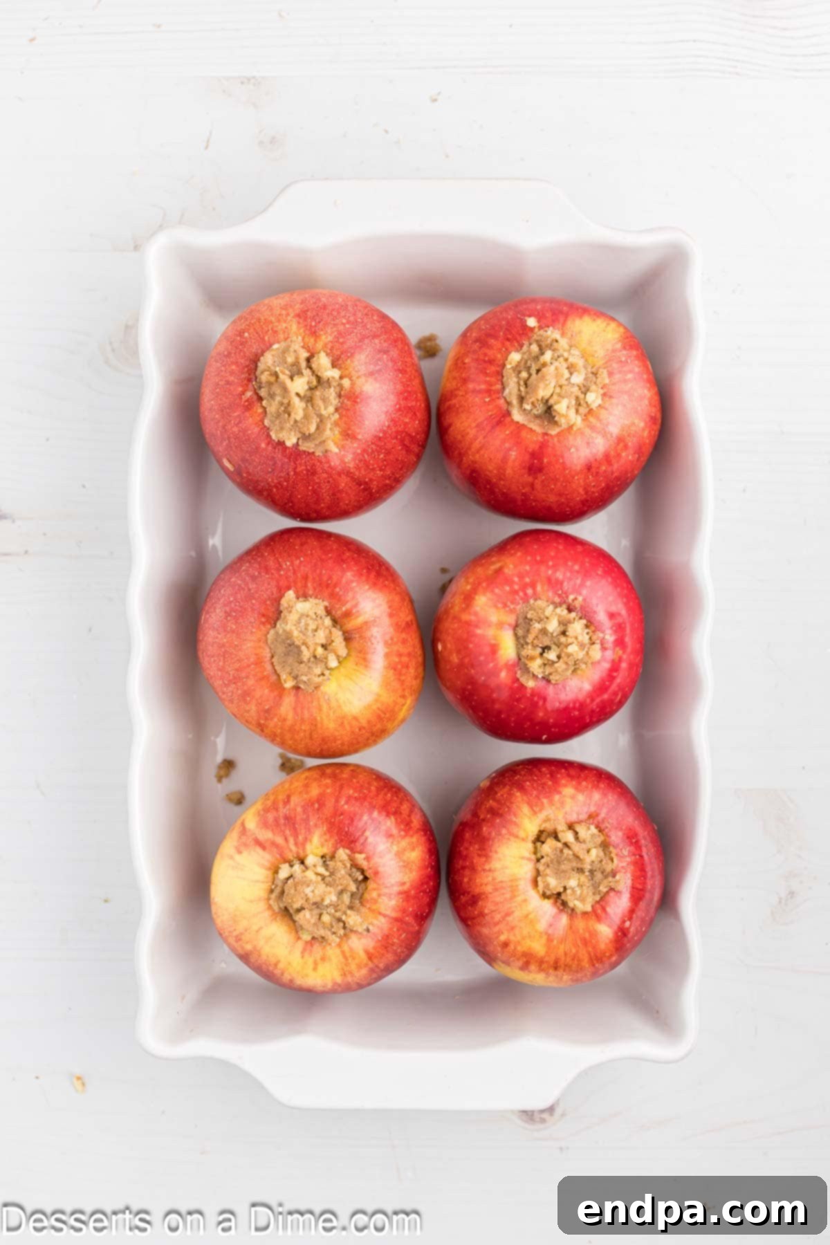 Cored apples filled with the cinnamon, brown sugar, butter, and walnut mixture, sitting in a baking dish with water at the bottom, ready for the oven.
