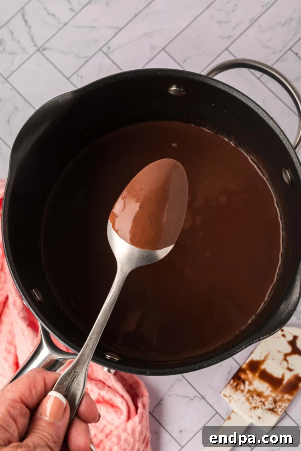 Velvety Dark Chocolate Pudding 6 The dark chocolate pudding mixture is shown thickening in a saucepan, with a spoon lifted to demonstrate how the rich, smooth pudding coats the back of it, indicating proper consistency.