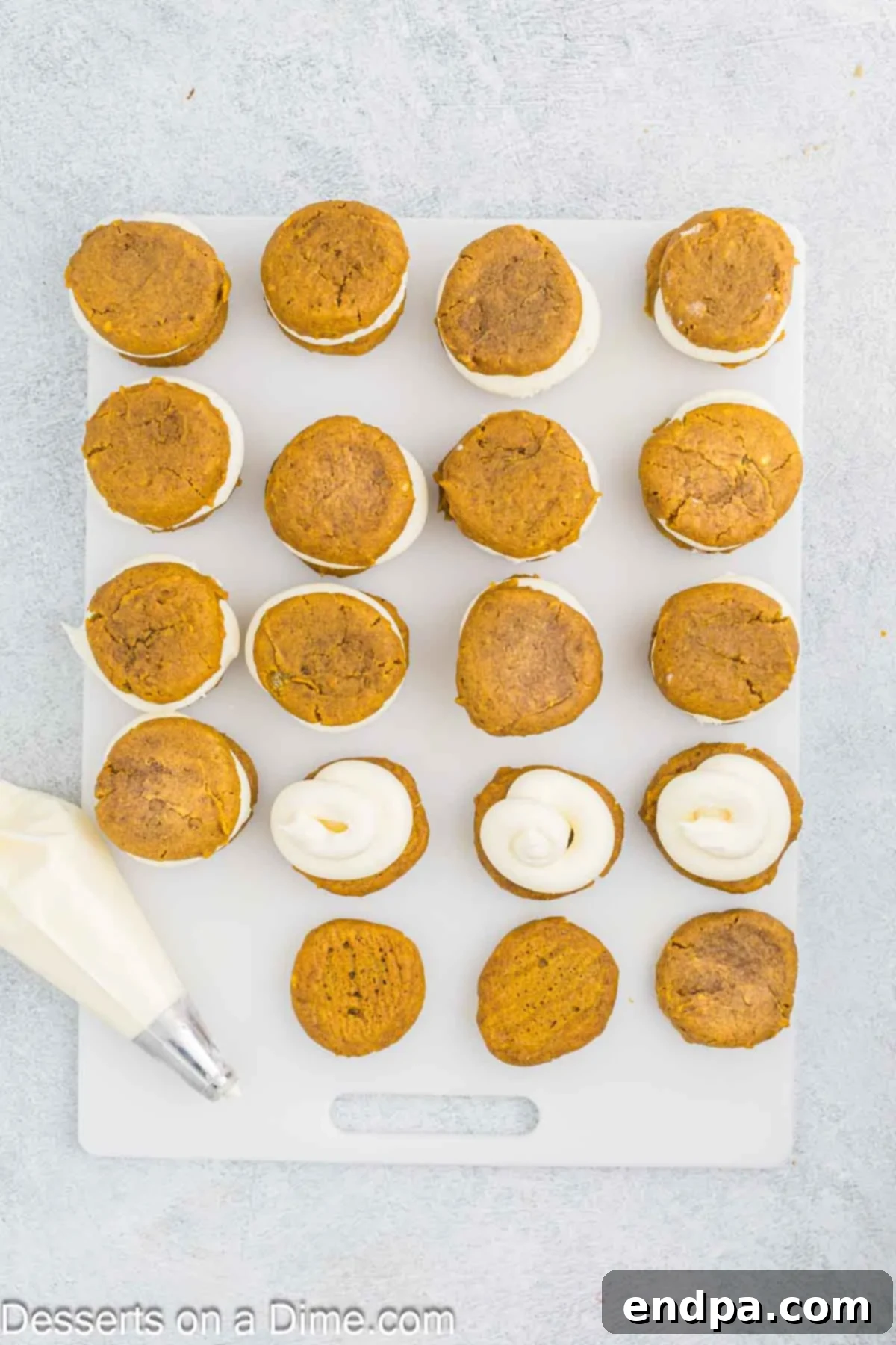 Autumn Pumpkin Cream Pies 11 A pumpkin whoopie pie being carefully assembled, with creamy white frosting piped onto the flat bottom of one cookie, ready to be topped by another cookie to form the sandwich.
