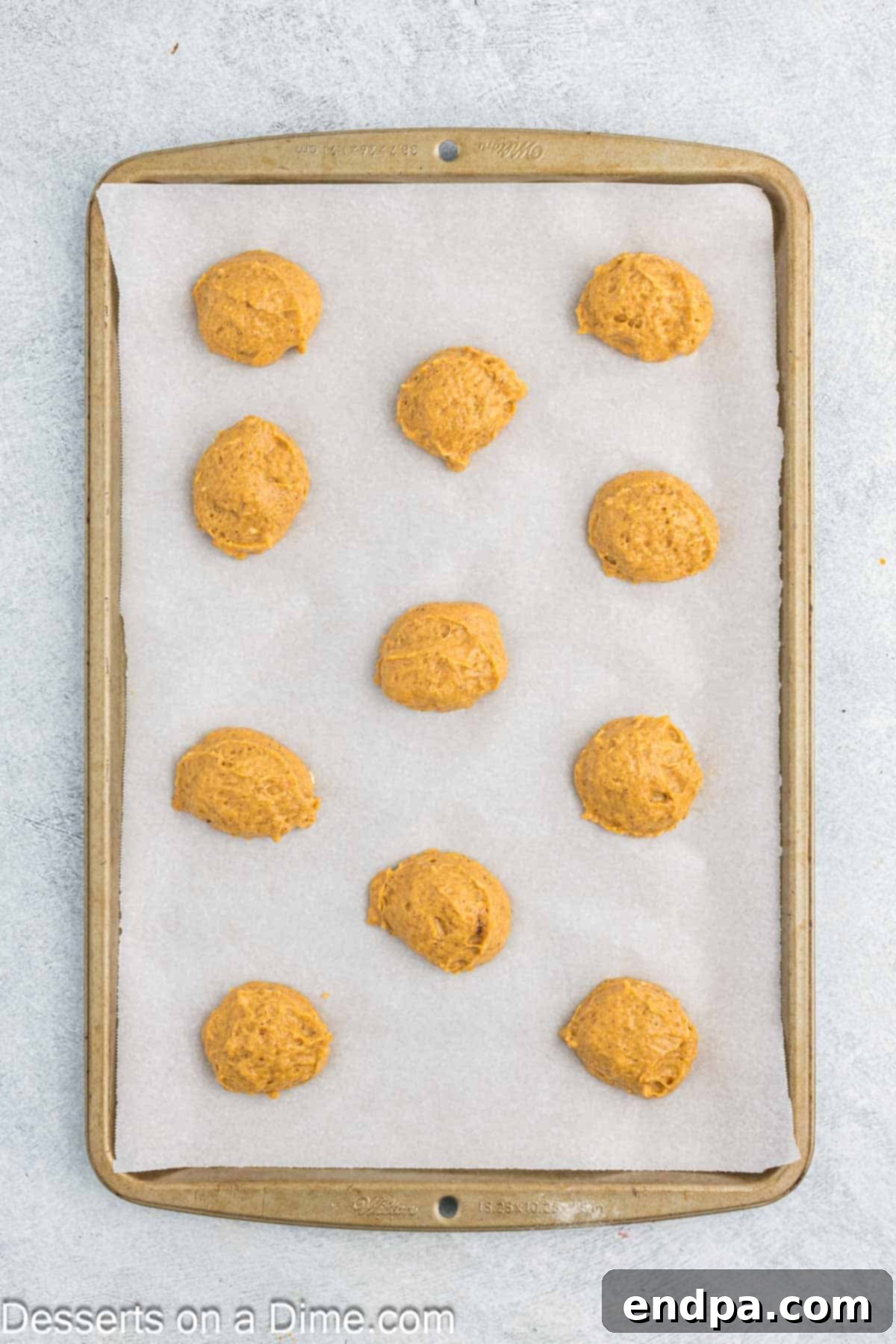 Autumn Pumpkin Cream Pies 7 Uniform scoops of pumpkin whoopie pie batter are neatly arranged on a parchment-lined baking sheet, demonstrating precise portioning for consistently sized and baked cookies.