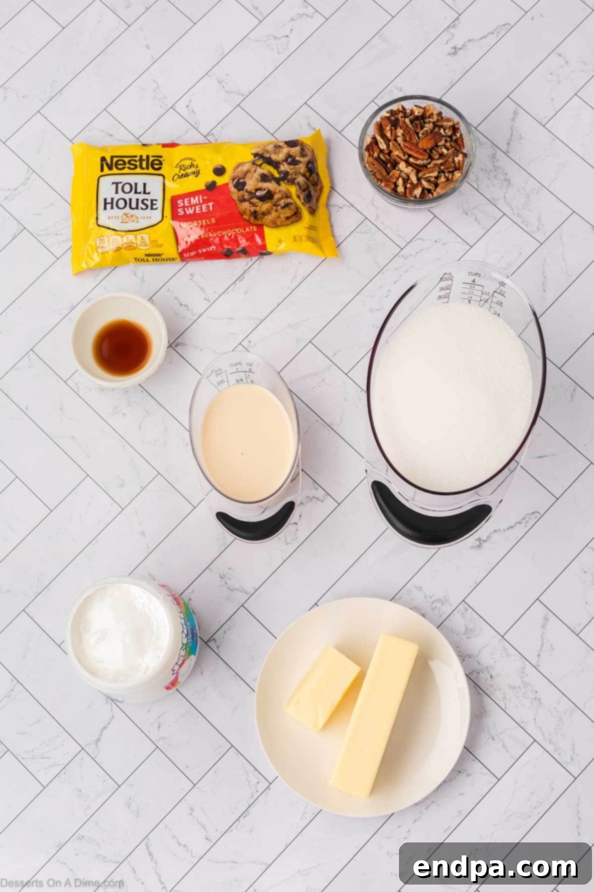 Arrangement of ingredients for Marshmallow Fluff Fudge, including butter, granulated sugar, evaporated milk, chocolate chips, marshmallow fluff, and chopped pecans, laid out on a clean surface.