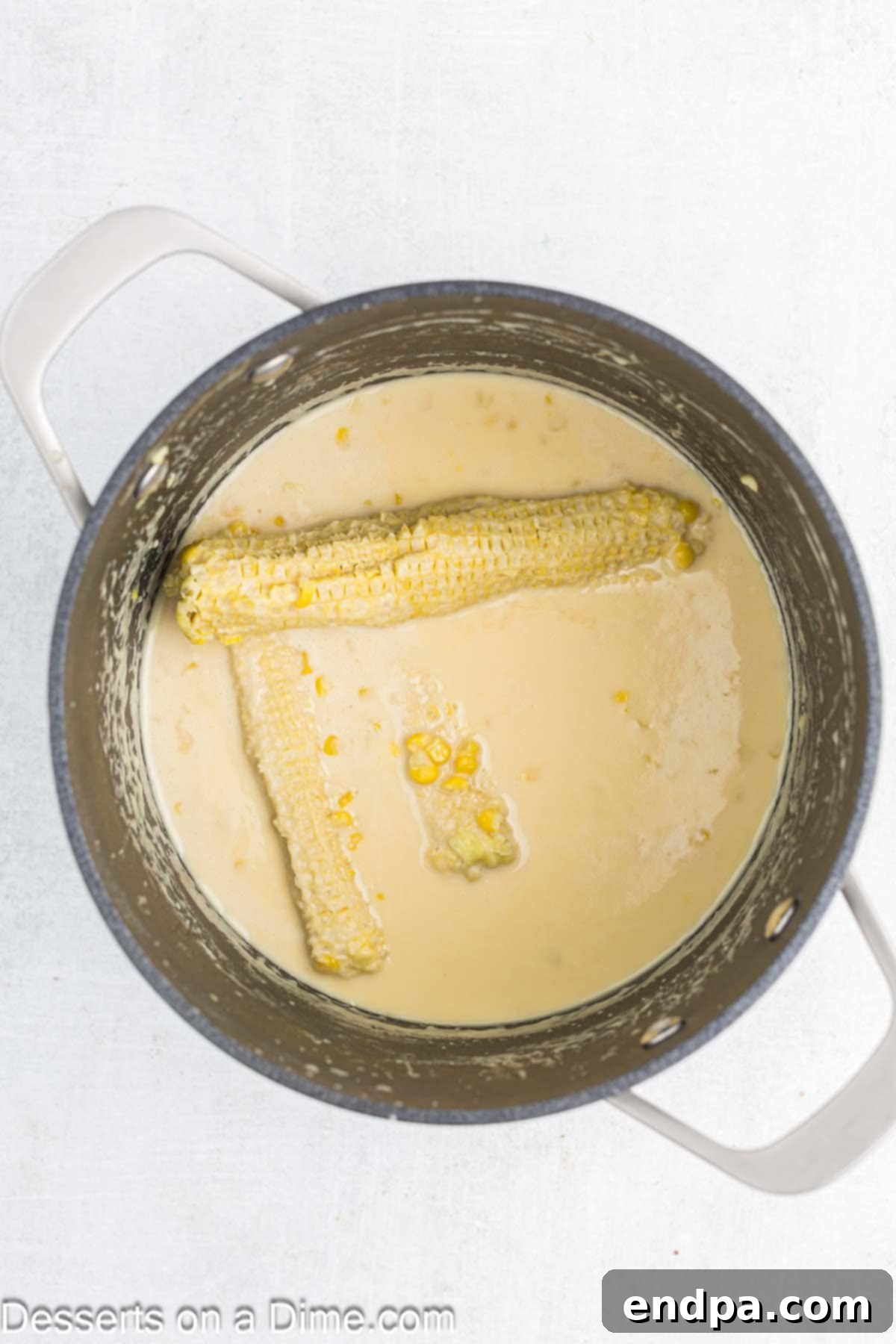 Corn kernels and cobs simmering in a milk mixture in a large pot.