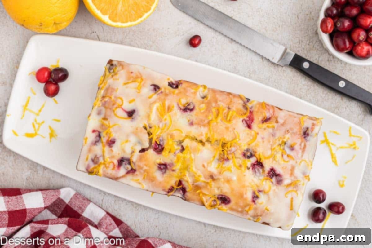 A freshly baked loaf of Orange Cranberry Bread on a rustic platter, garnished with fresh cranberries and orange slices.