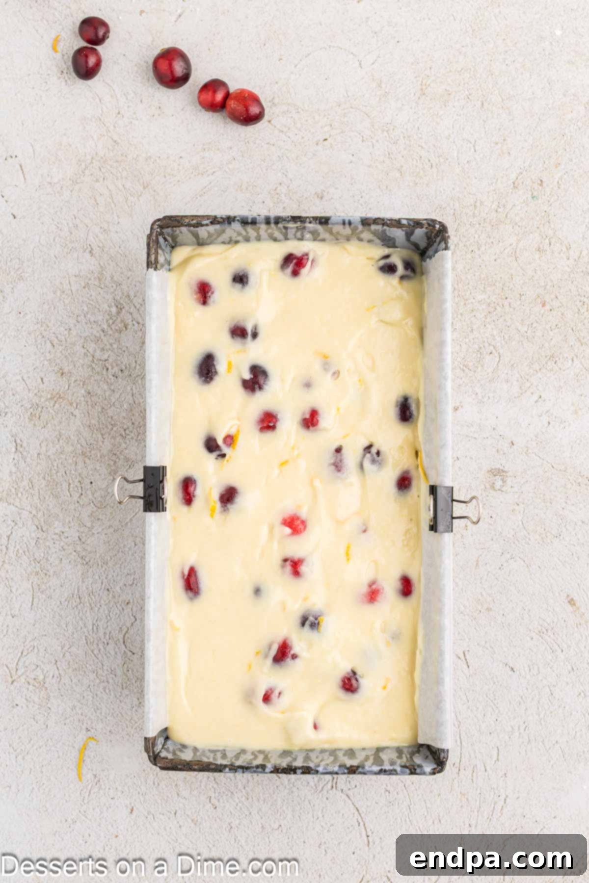 Orange cranberry bread batter, with fresh cranberries visible, poured into a parchment-lined loaf pan, ready for baking.
