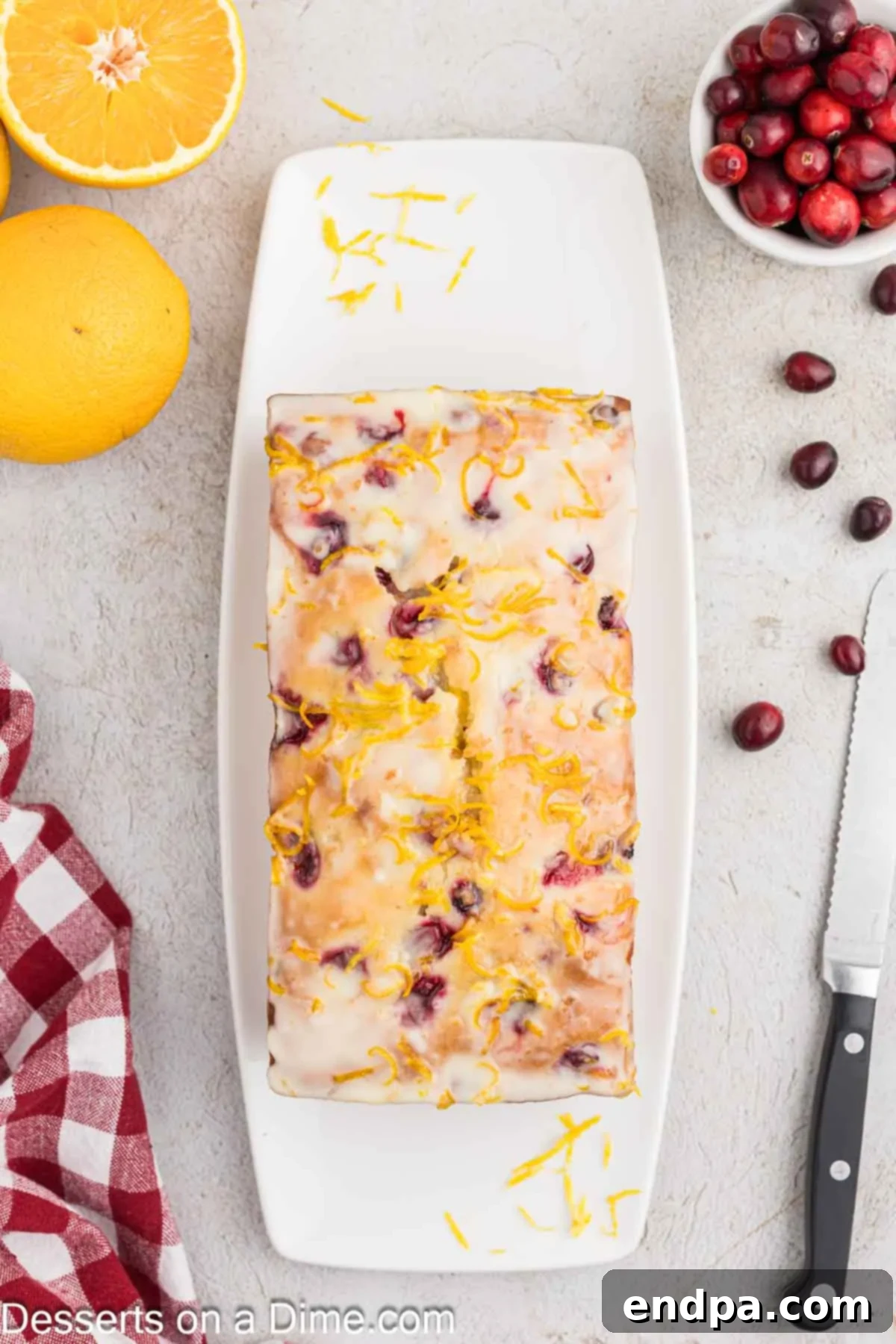 Orange cranberry bread on a wire rack being drizzled with a smooth orange glaze, showing a glossy finish.