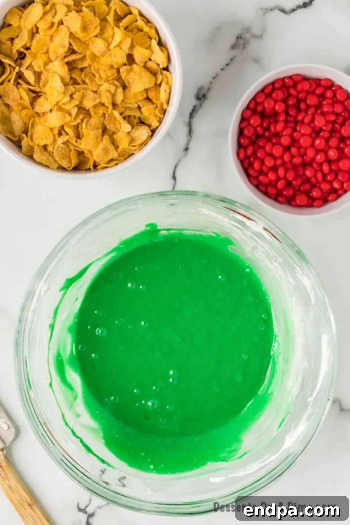 Green gel food coloring being carefully added to the warm, melted marshmallow and butter mixture.