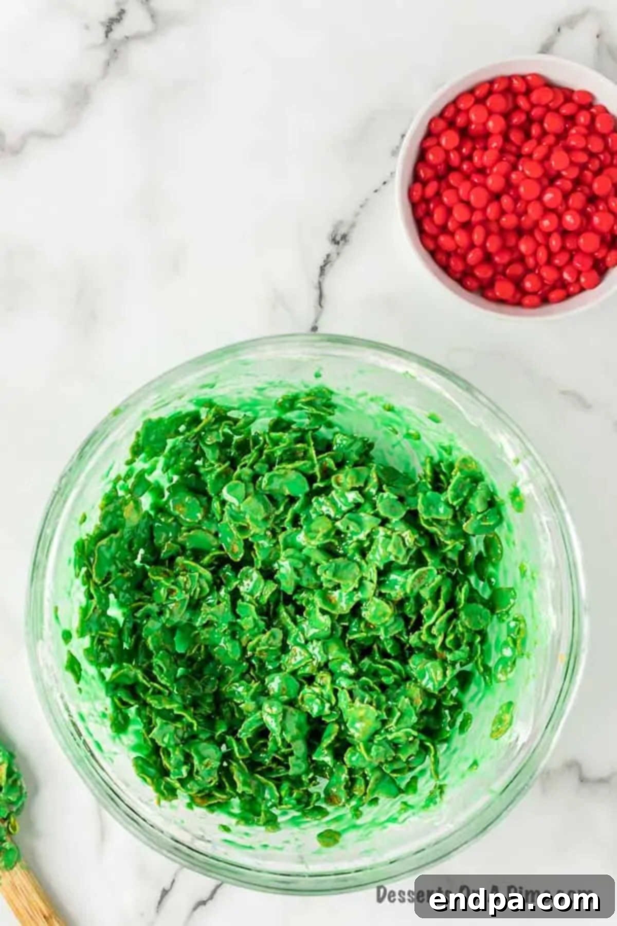 Cornflake cereal being gently folded into the bright green marshmallow mixture in a large mixing bowl.