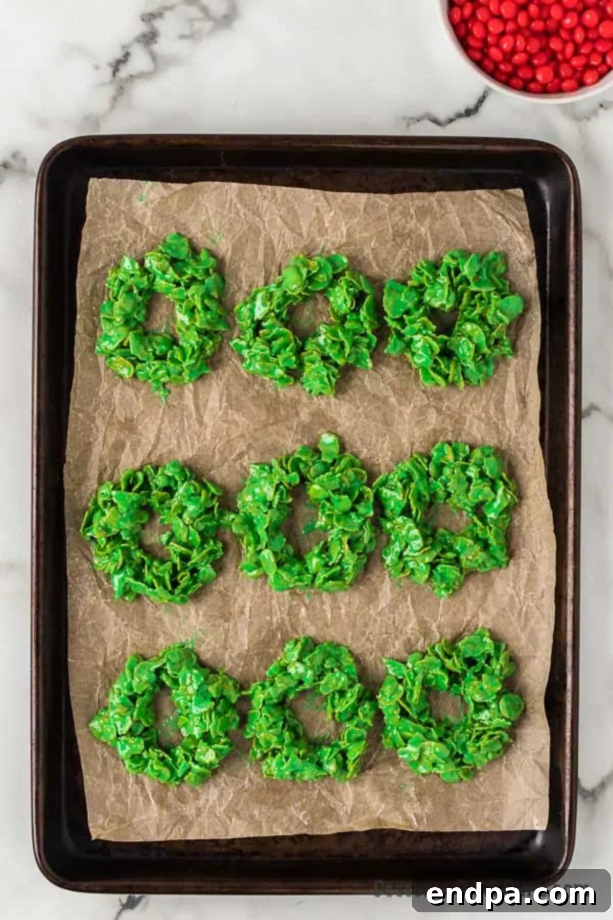 Several wreath shapes made from the cornflake mixture, neatly arranged on a baking sheet lined with parchment paper.