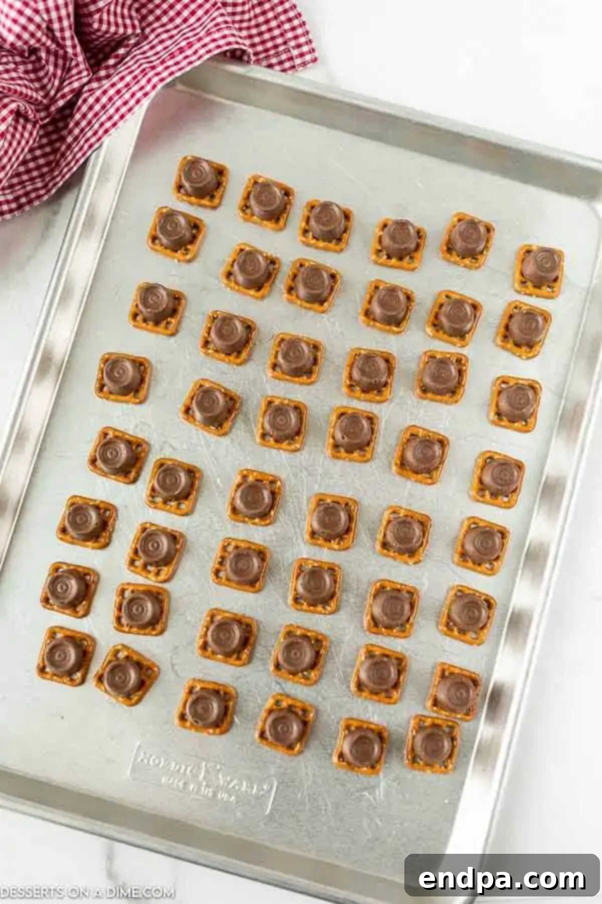 Baking sheet with pretzels topped with Rolo candies, ready for the oven.