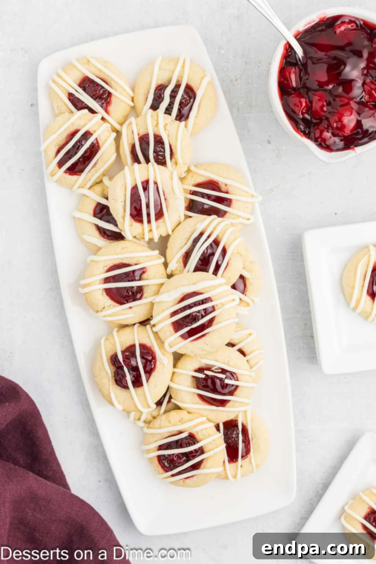 Crimson Cherry Thumbprint Cookies 12 A festive white tray filled with beautifully arranged Cherry Thumbprint cookies, each showcasing its glossy cherry filling and white chocolate drizzle.