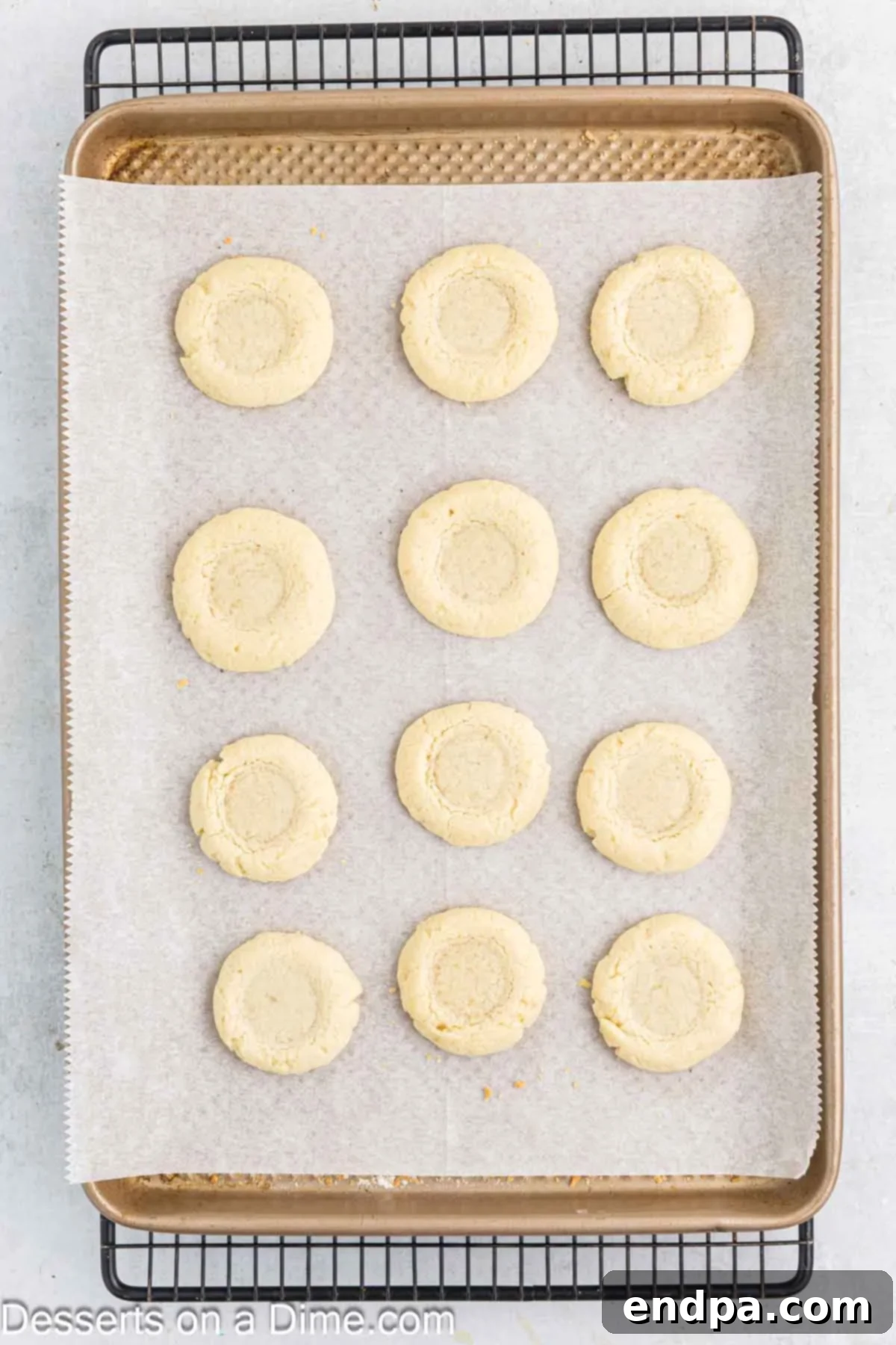 Crimson Cherry Thumbprint Cookies 8 Freshly baked thumbprint cookies, lightly golden, cooling on a baking sheet after their initial bake, with indentations visible.