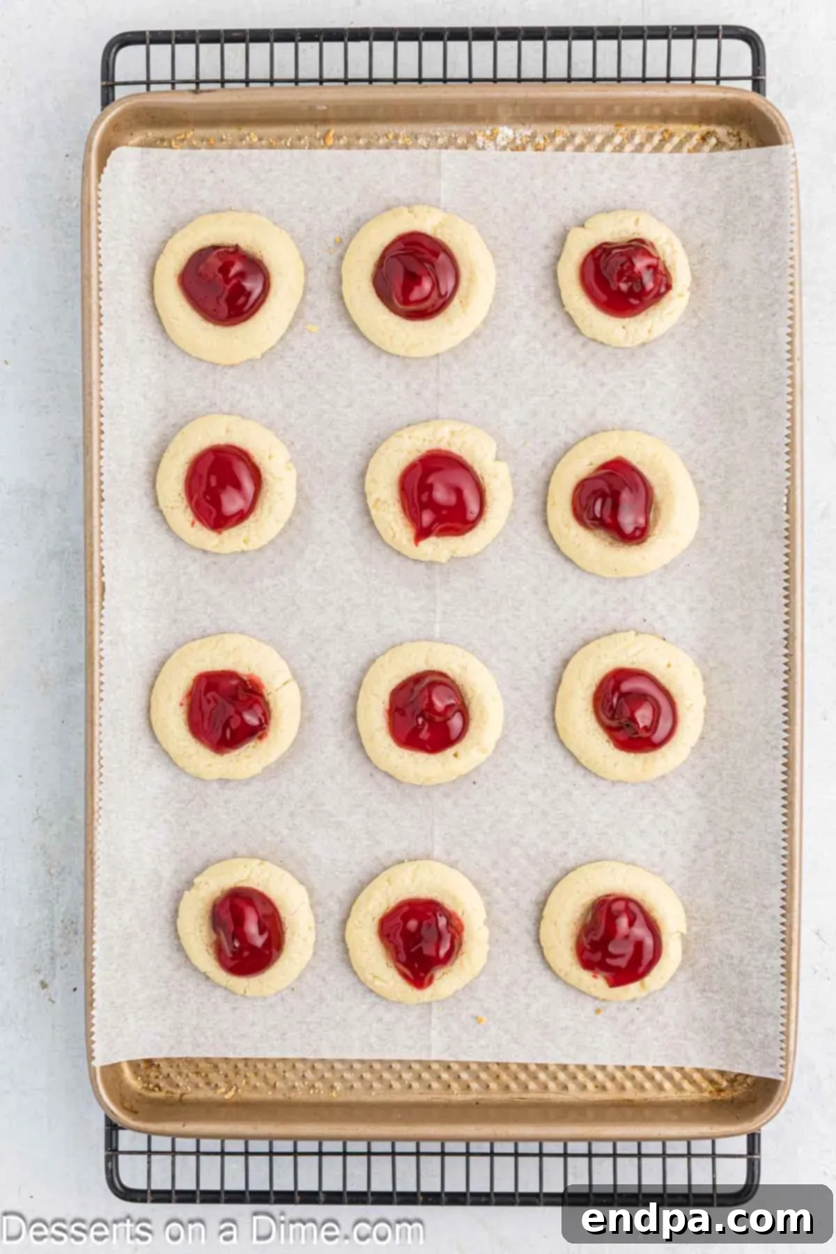 Crimson Cherry Thumbprint Cookies 9 Cherry pie filling carefully spooned into the warm indentations of baked thumbprint cookies on a baking sheet, ready for a final short bake.