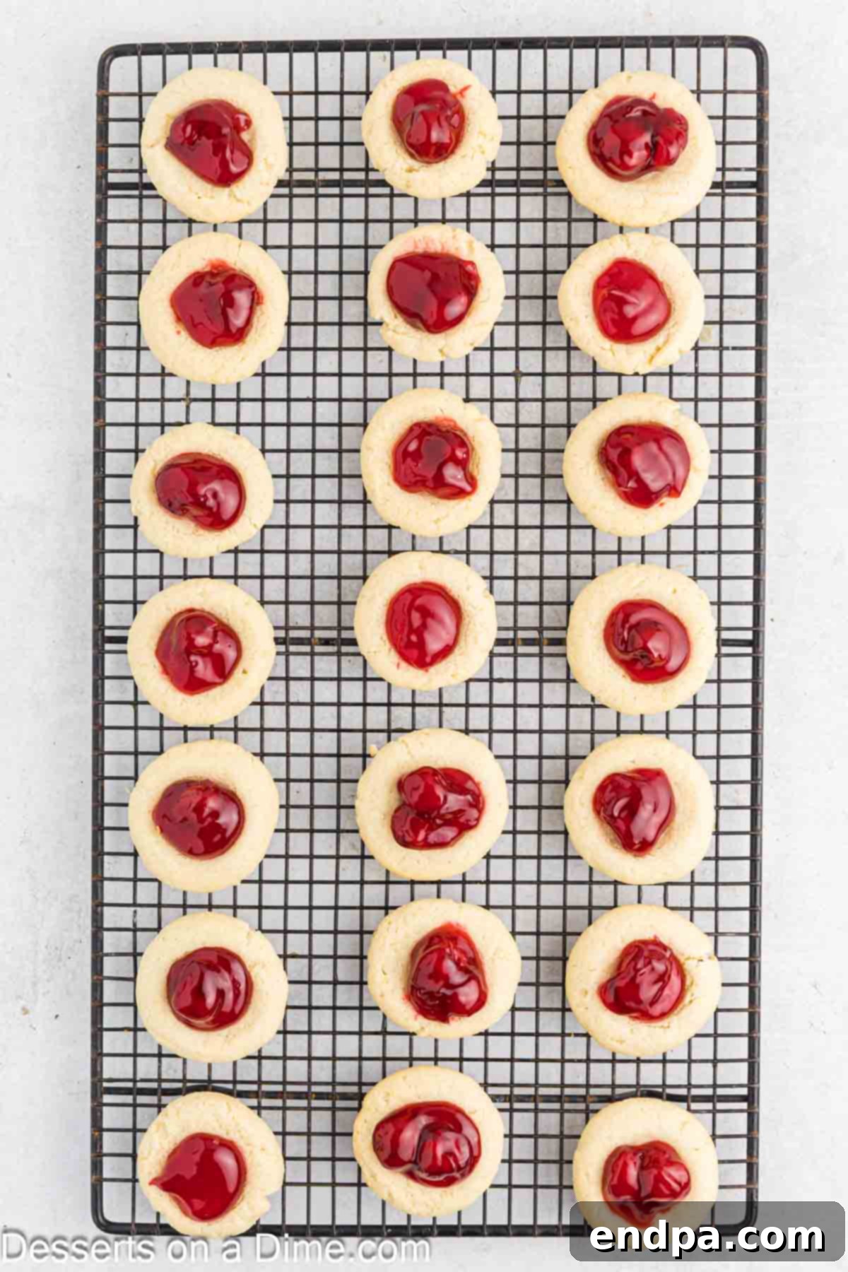 Crimson Cherry Thumbprint Cookies 10 Baked Cherry Thumbprint cookies cooling completely on a wire rack, allowing them to set and firm up.