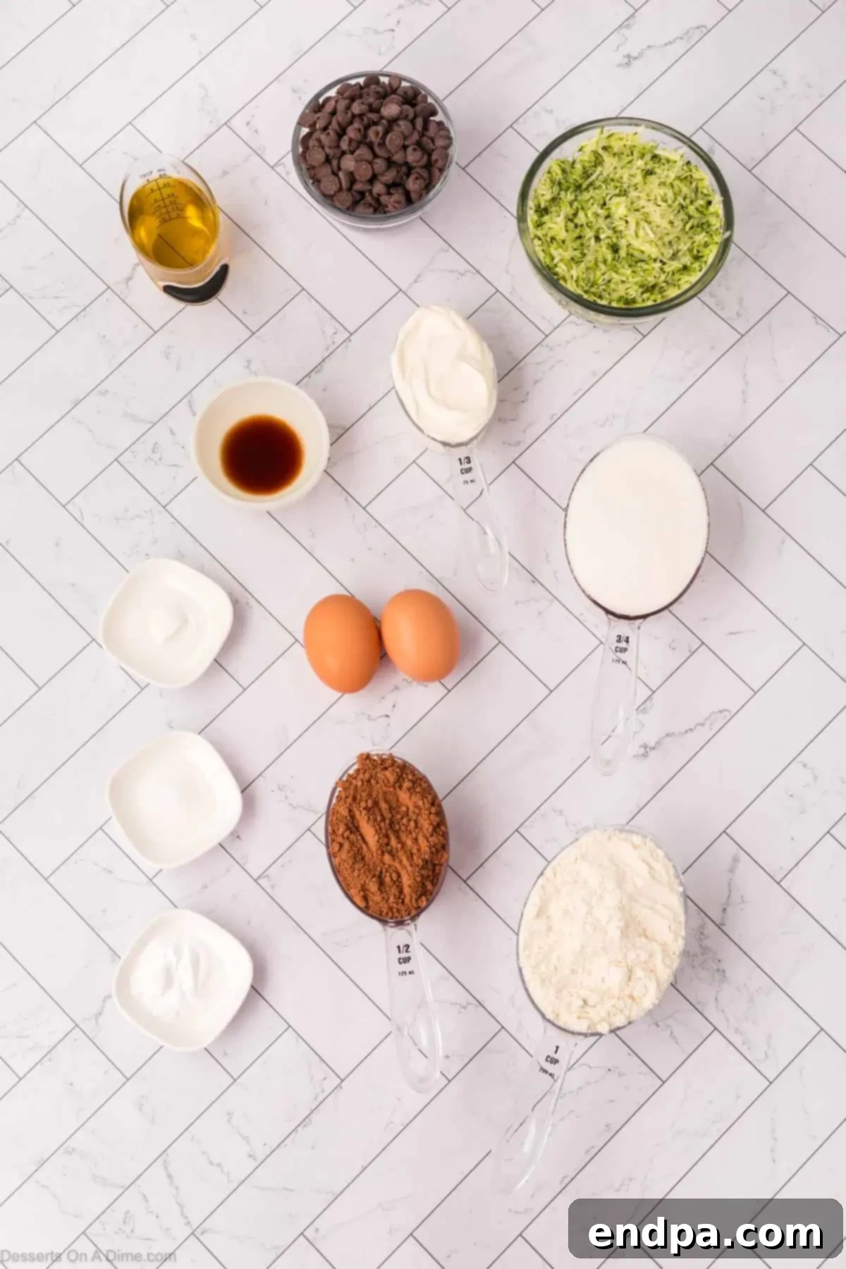 A collection of ingredients for Chocolate Zucchini Bread, including flour, cocoa powder, chocolate chips, eggs, oil, sour cream, sugar, vanilla, and of course, zucchini.