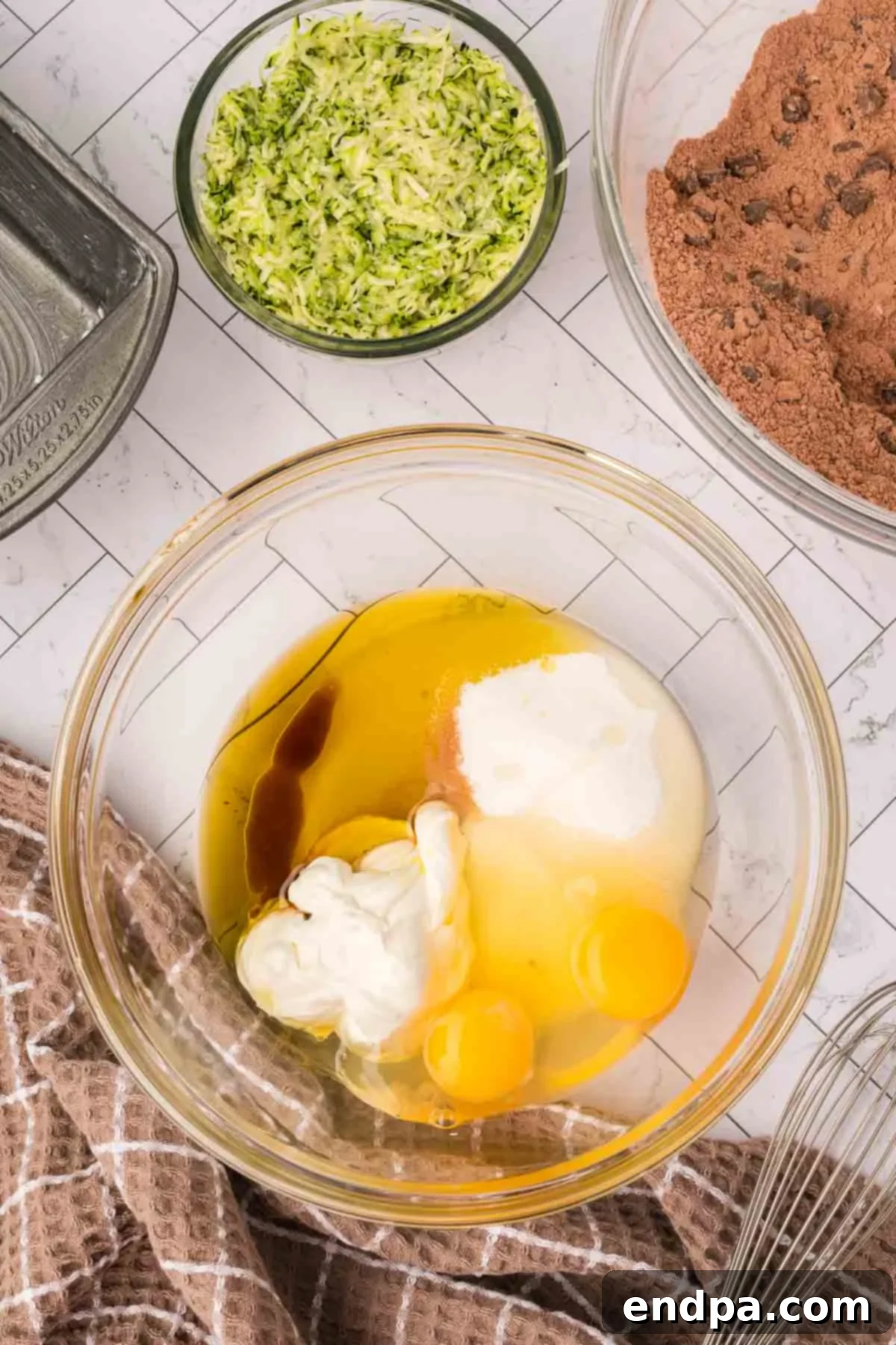 Wet ingredients in a separate mixing bowl, ready to be combined, including eggs, oil, sour cream, sugar, and vanilla extract.