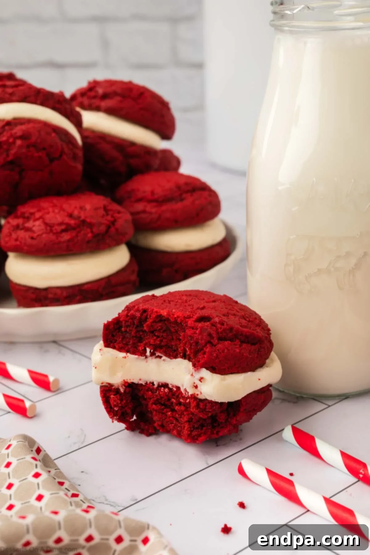 Finished Red Velvet sandwich cookies stacked together on a platter next to a glass of milk.