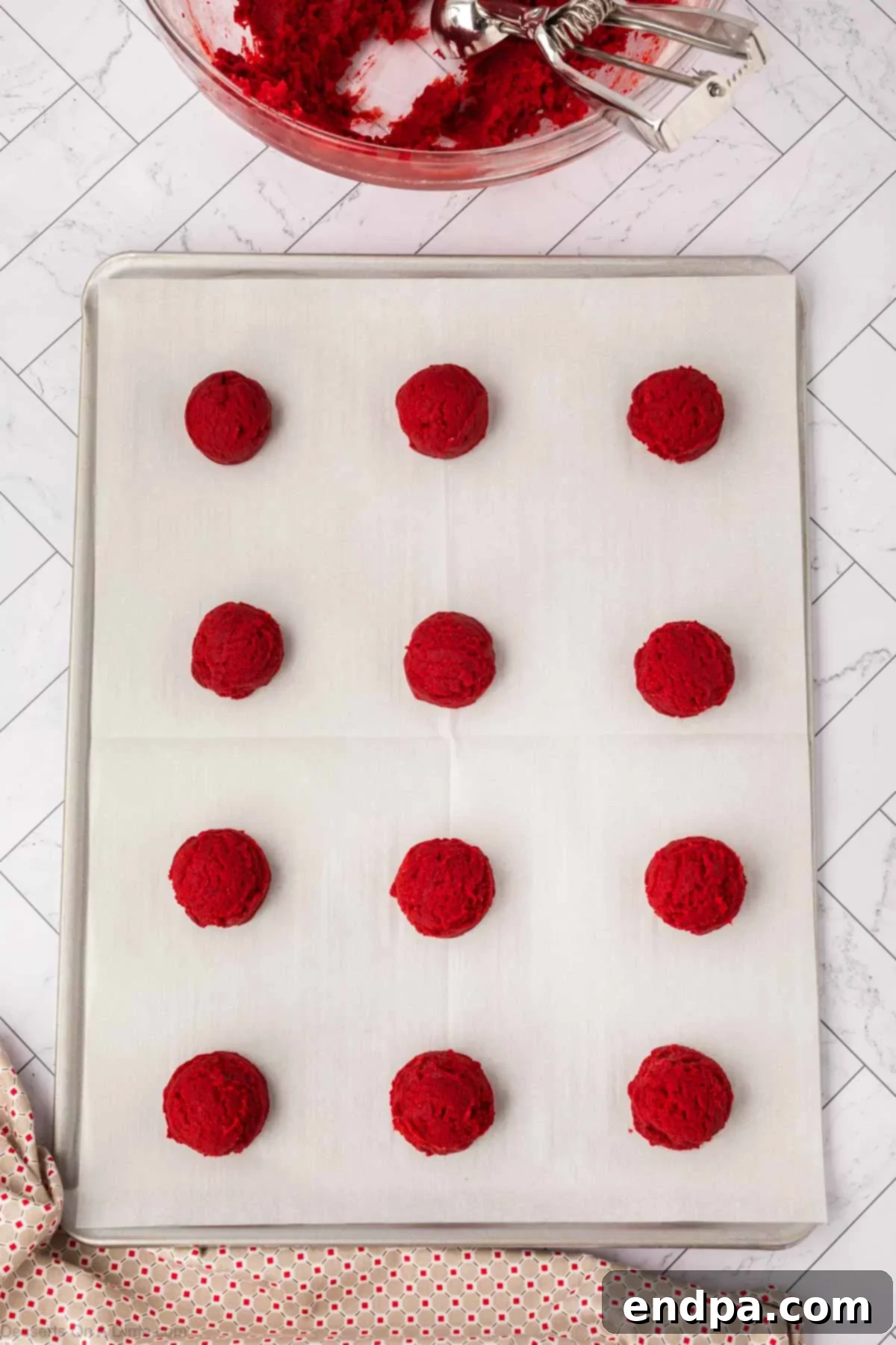 Scooped portions of red velvet cookie dough placed on a prepared baking sheet.