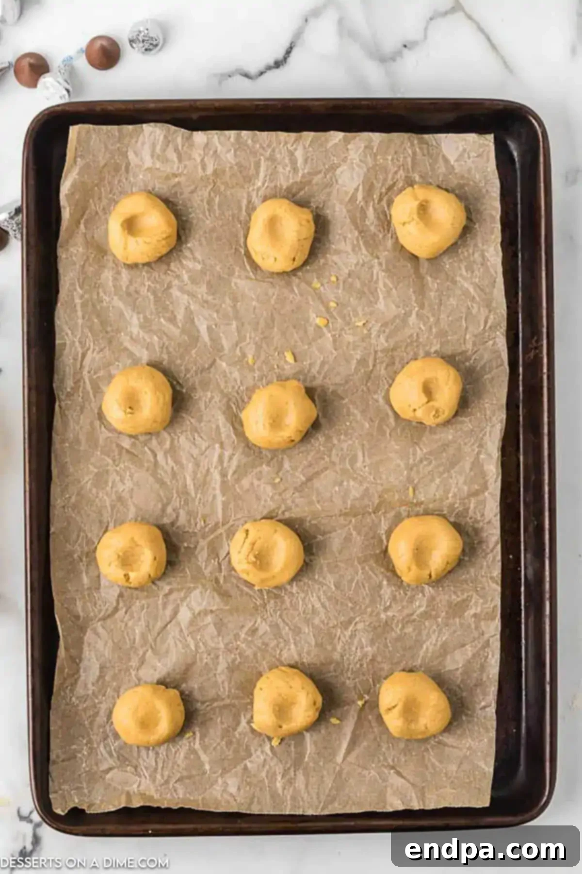 Peanut butter cookie dough balls, each with a gentle indentation in the center, arranged on an ungreased baking sheet.