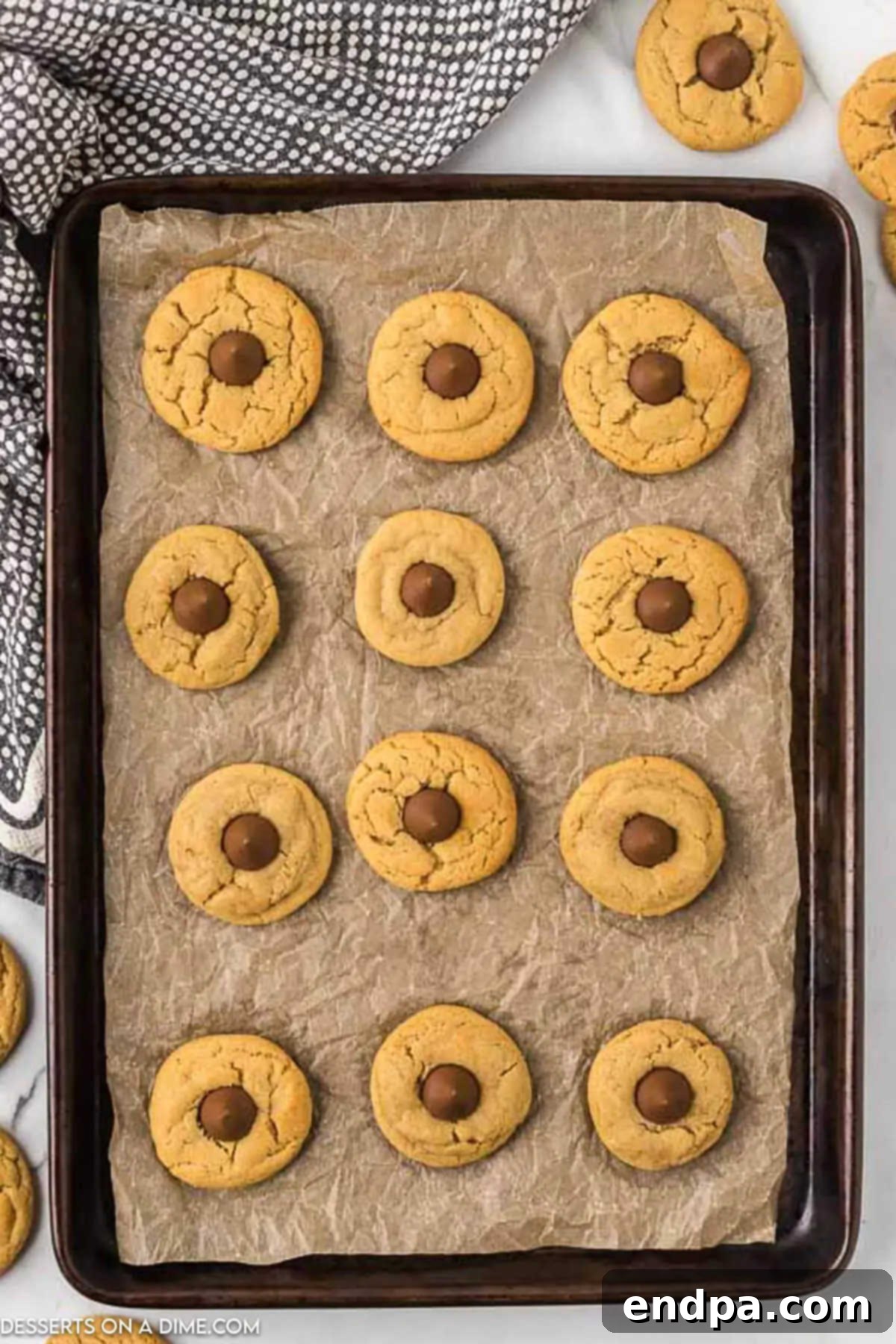 Warm, freshly baked Peanut Butter Kiss Cookies on a baking sheet with Hershey's Kisses pressed into their centers.
