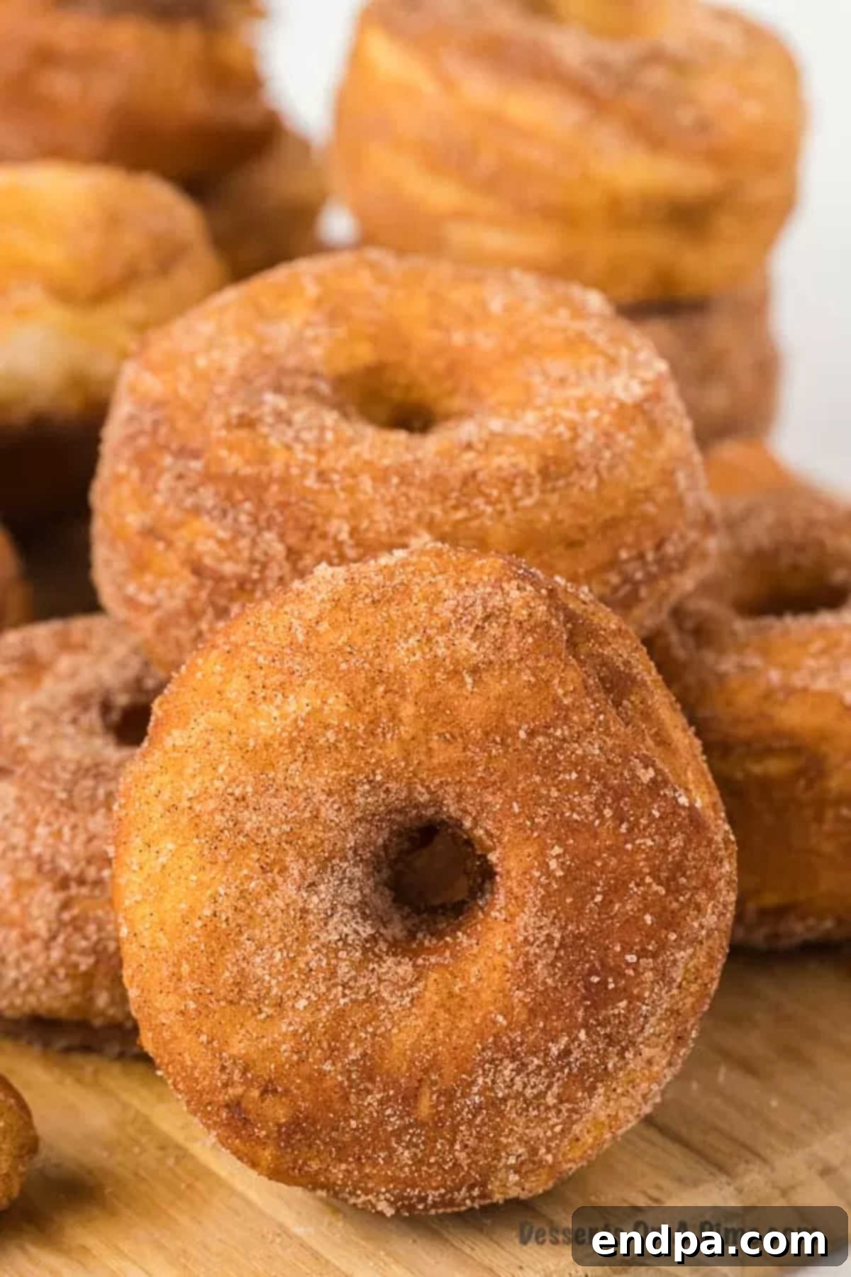 Freshly made biscuit donuts generously coated with a sparkling cinnamon and sugar mixture, presented on a white plate ready to be enjoyed.