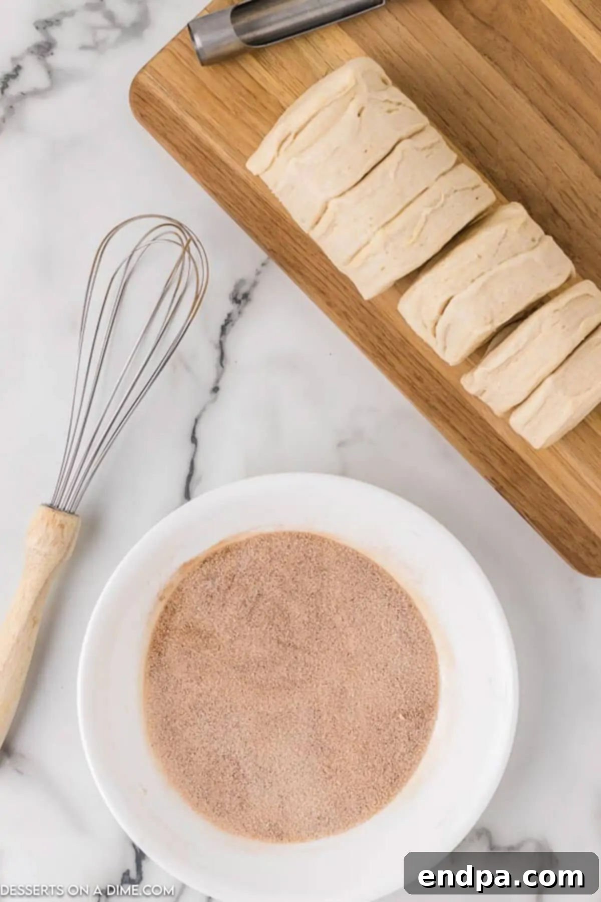 A small glass bowl holding a perfectly mixed cinnamon sugar topping, positioned next to an unopened tube of refrigerated biscuits on a wooden surface.
