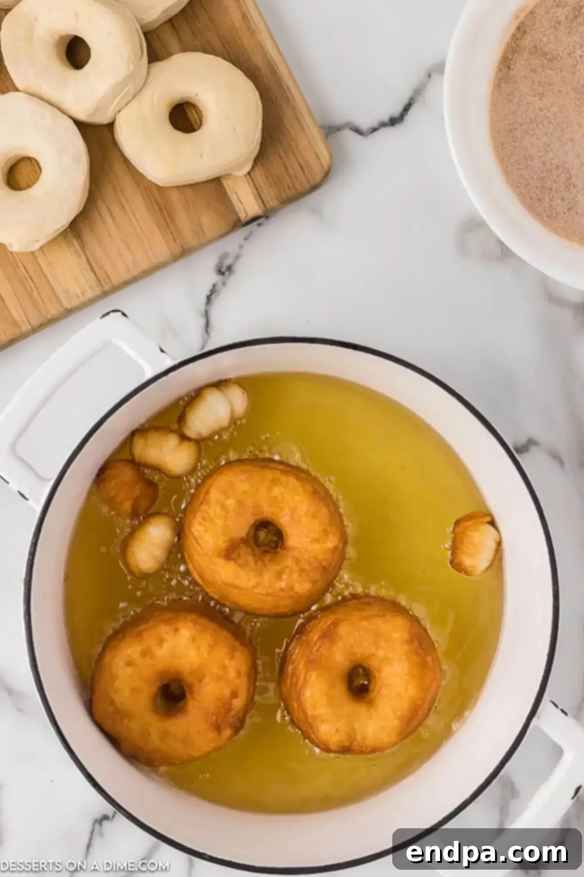 Three biscuit donuts submerged in shimmering hot vegetable oil, frying to a perfect golden brown in a small saucepan.