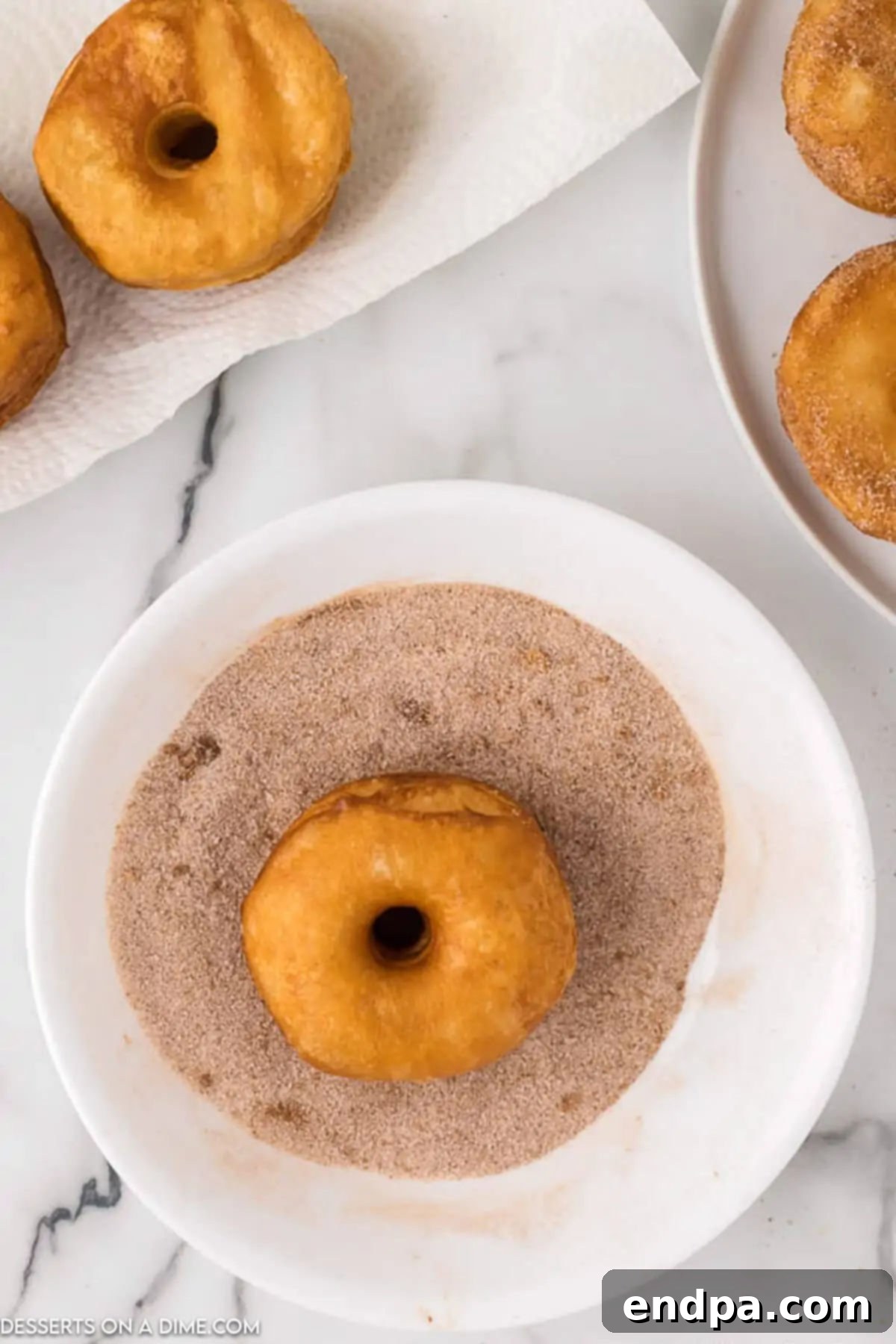 A freshly fried, golden-brown biscuit donut being generously coated in a bowl filled with a cinnamon sugar mixture.