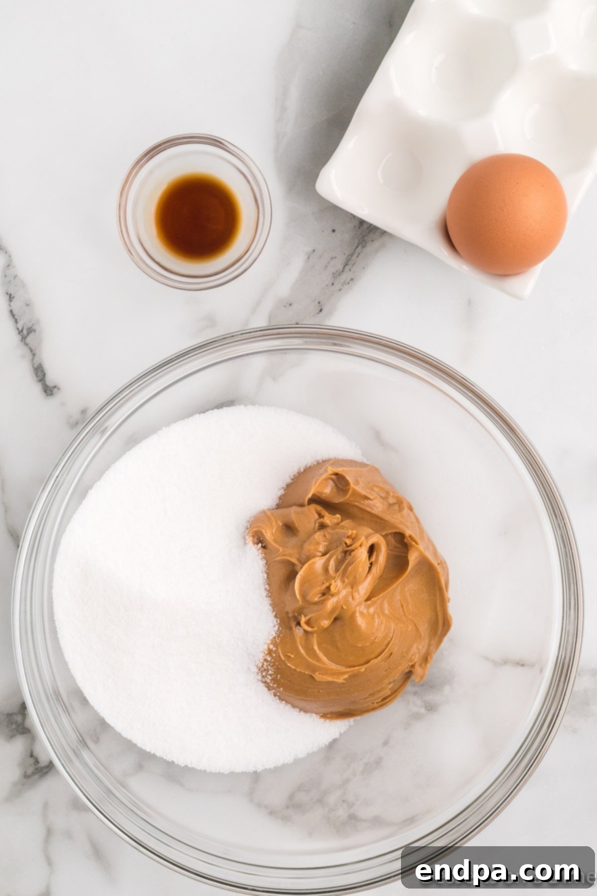 Decadent Keto Peanut Butter Cookies 4 Mixing bowl with creamy peanut butter, Swerve sweetener, a cracked egg, and a splash of vanilla extract.