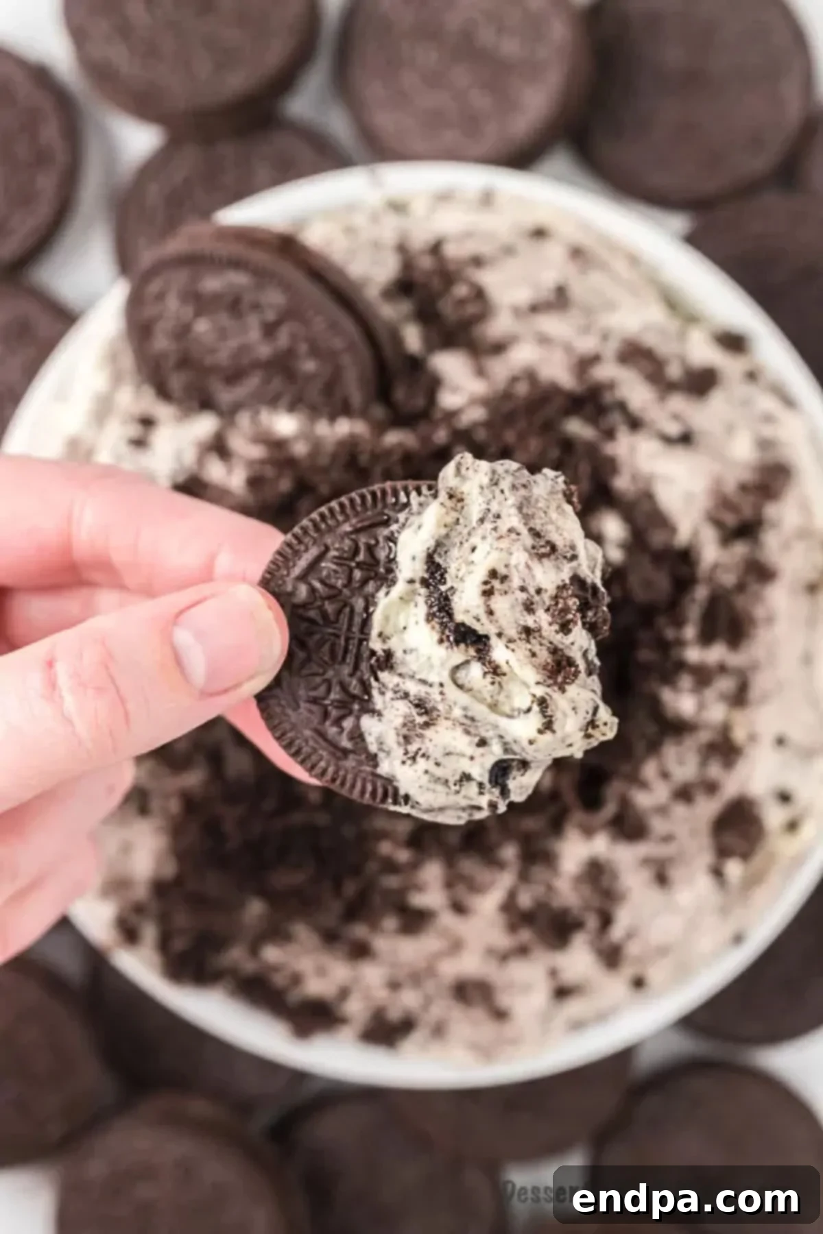 Bowl of Oreo Fluff with someone dipping into the bowl with a whole Oreo cookie.