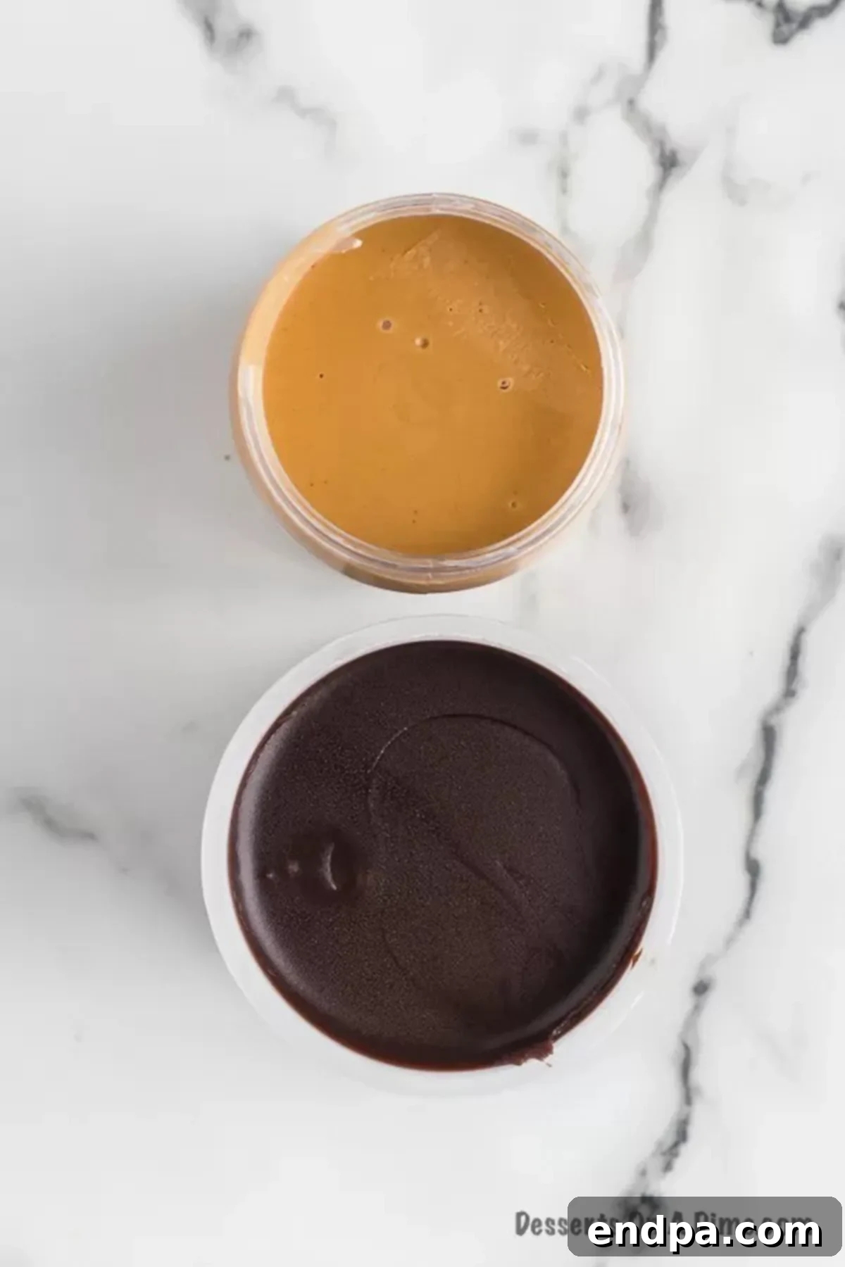Two jars on a white surface: one filled with creamy peanut butter, the other with chocolate frosting.